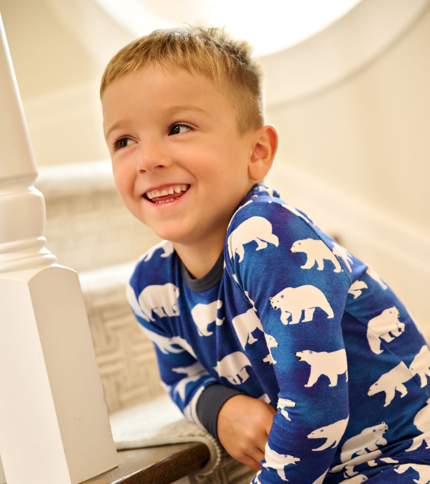 Blue bamboo pajama set featuring white polar bear patterns, worn by a smiling boy sitting on stairs.