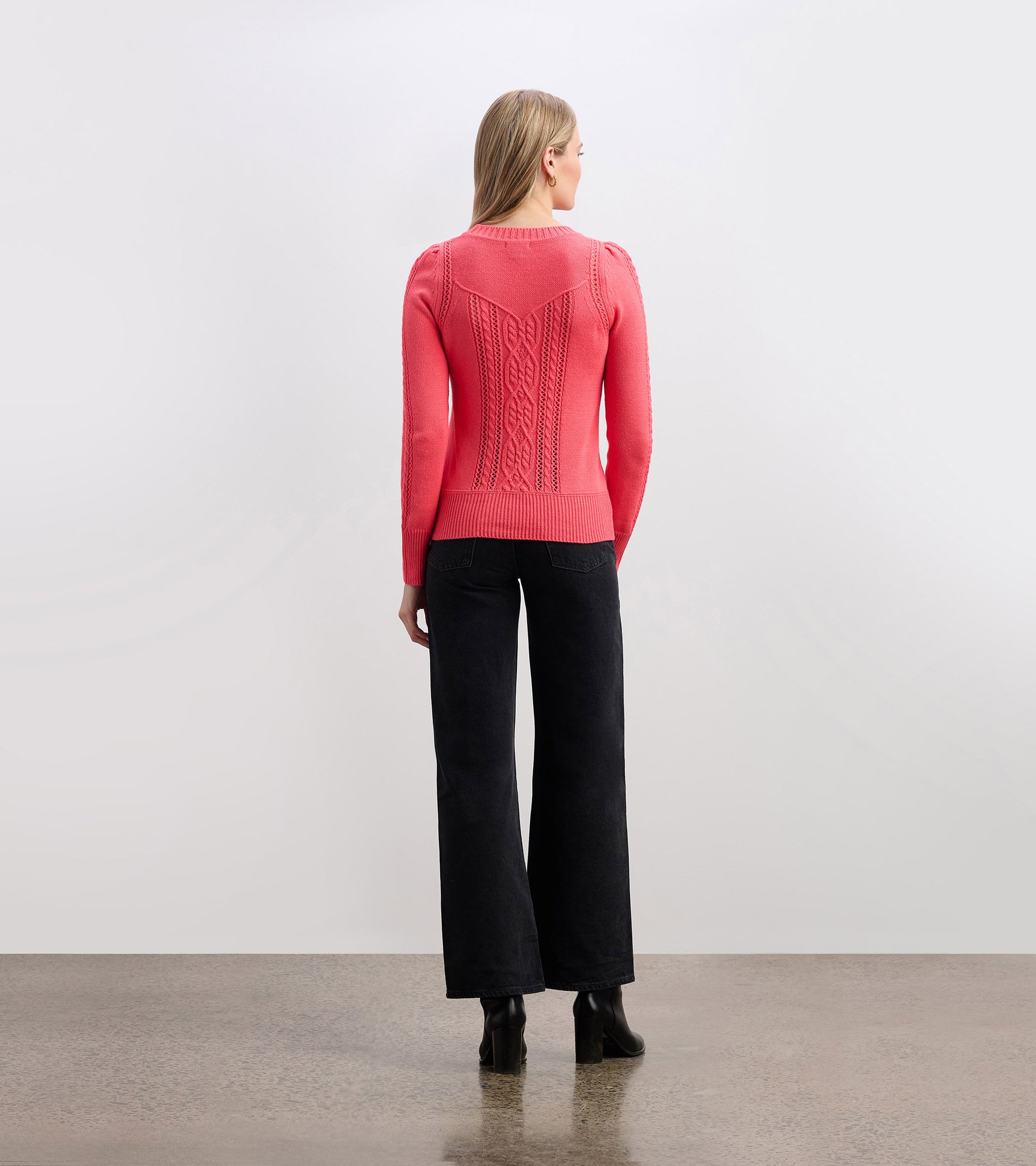 Neon melon sweater with textured cable knit design, fitted at the waist, shown from the back with black wide-leg pants.