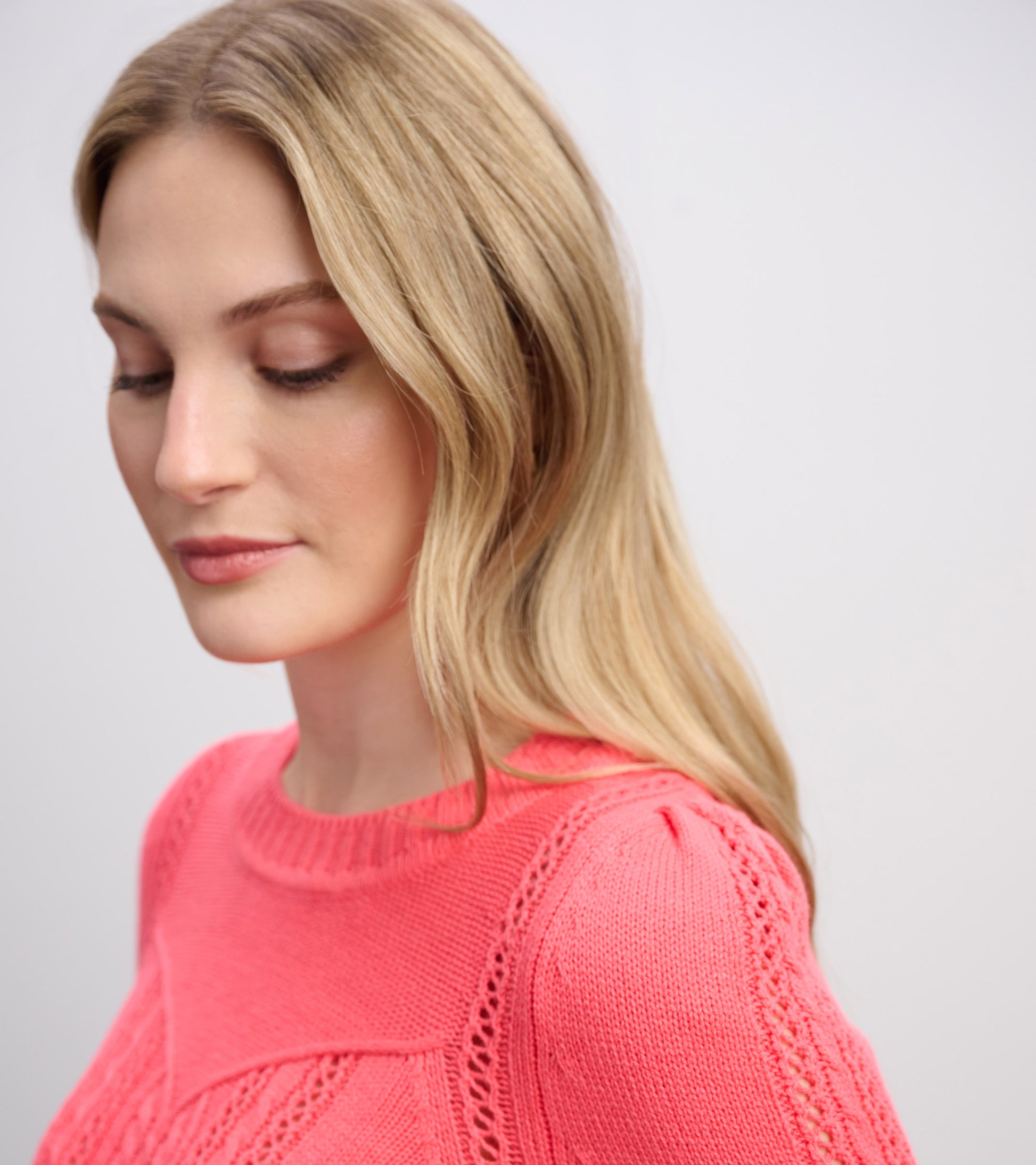 Neon melon sweater with a textured pattern and a round neckline, styled on a model with long, wavy hair.