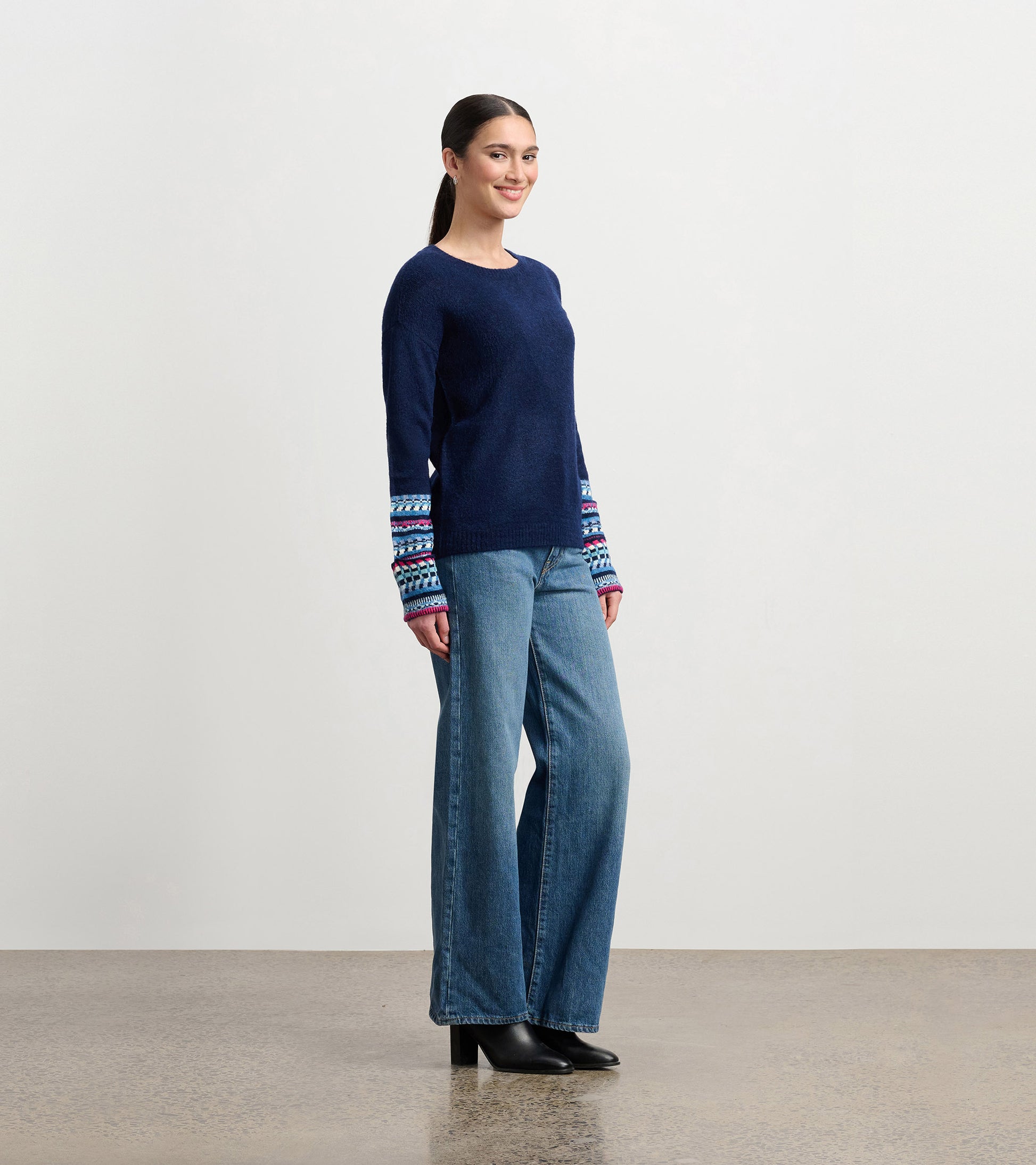 Navy sweater with colorful jacquard cuffs, featuring a relaxed fit and round neckline, paired with wide-leg jeans.