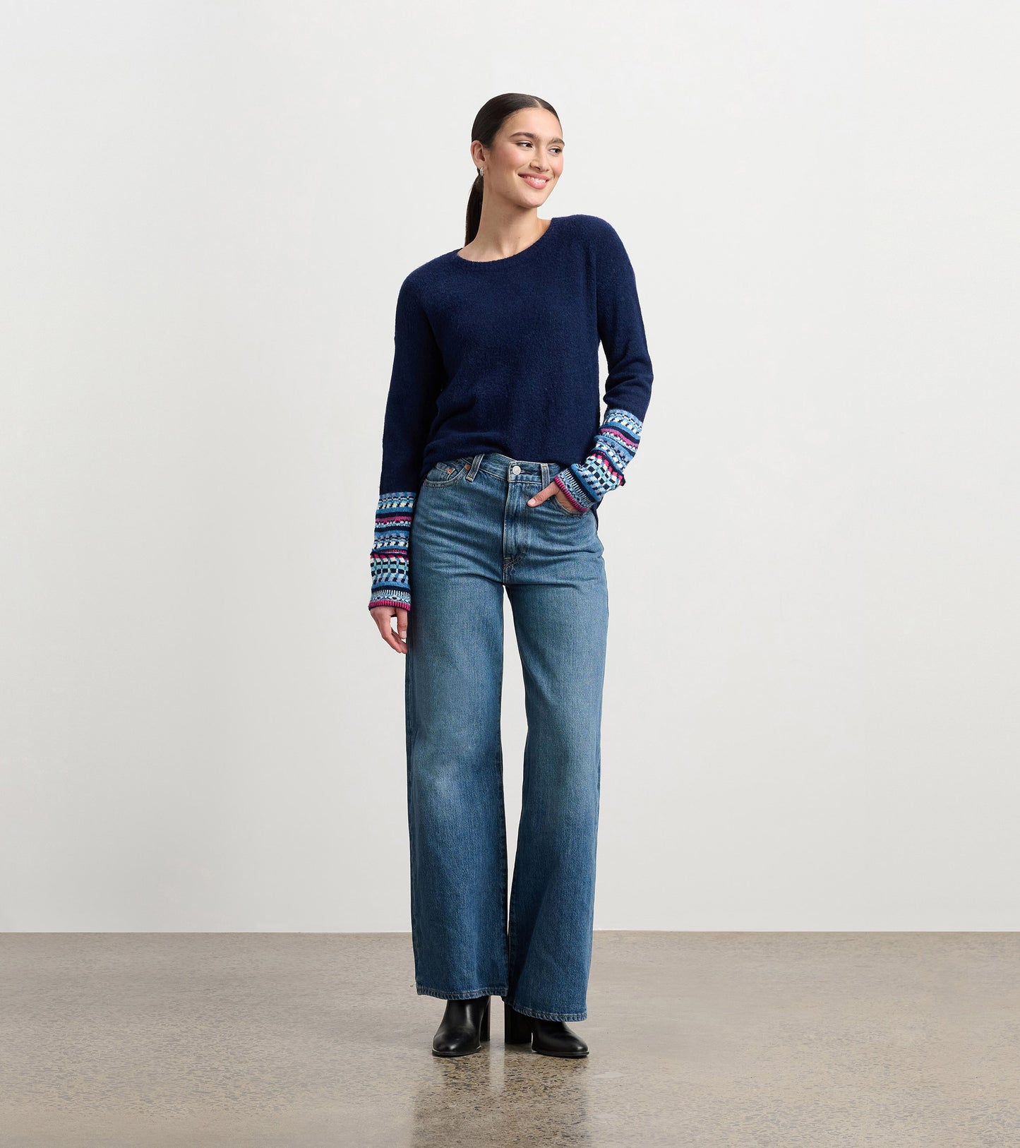 Navy sweater with patterned cuffs, paired with high-waisted jeans, worn by a model standing and smiling.
