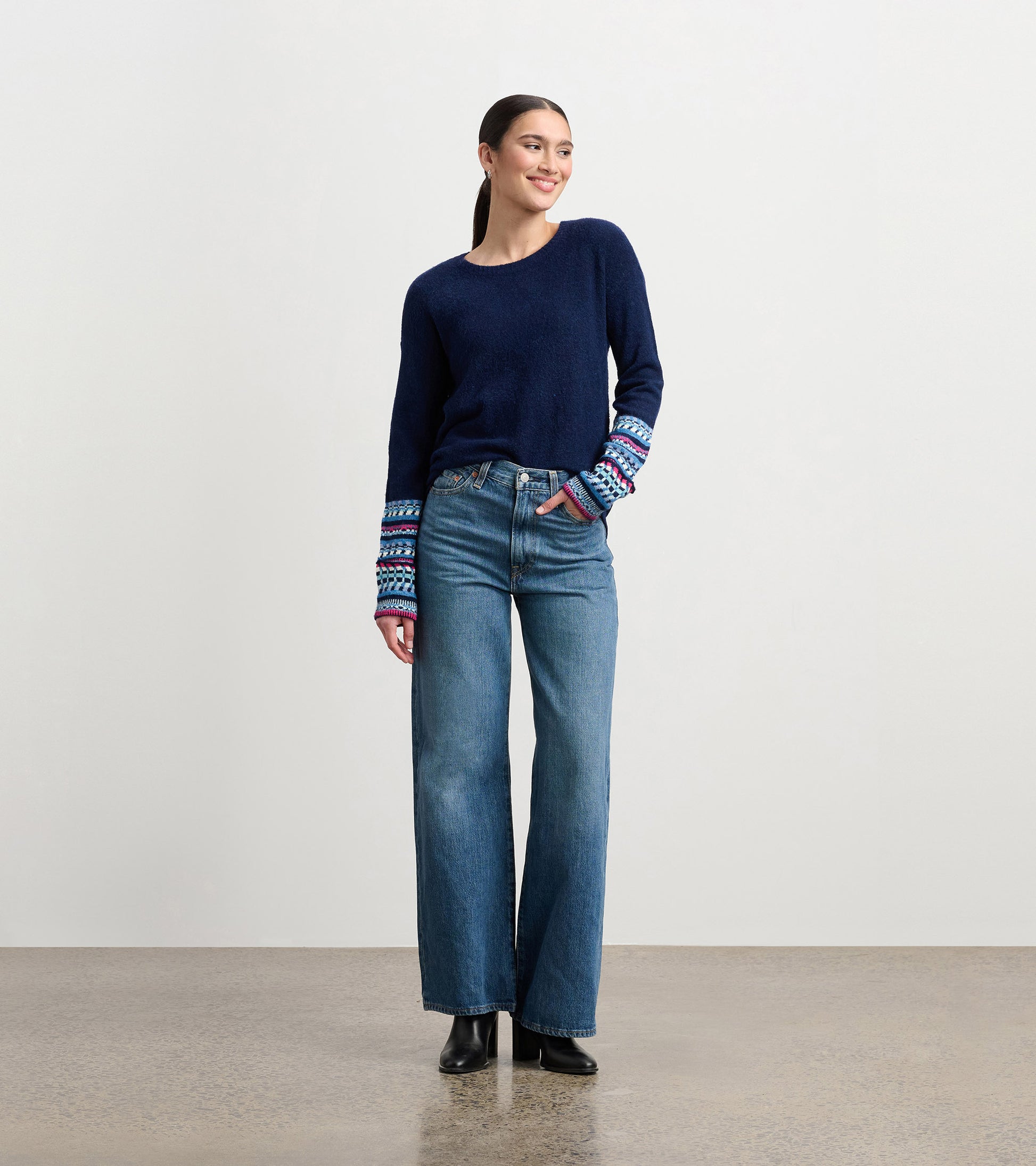 Navy sweater with patterned cuffs, paired with high-waisted jeans, worn by a model standing and smiling.