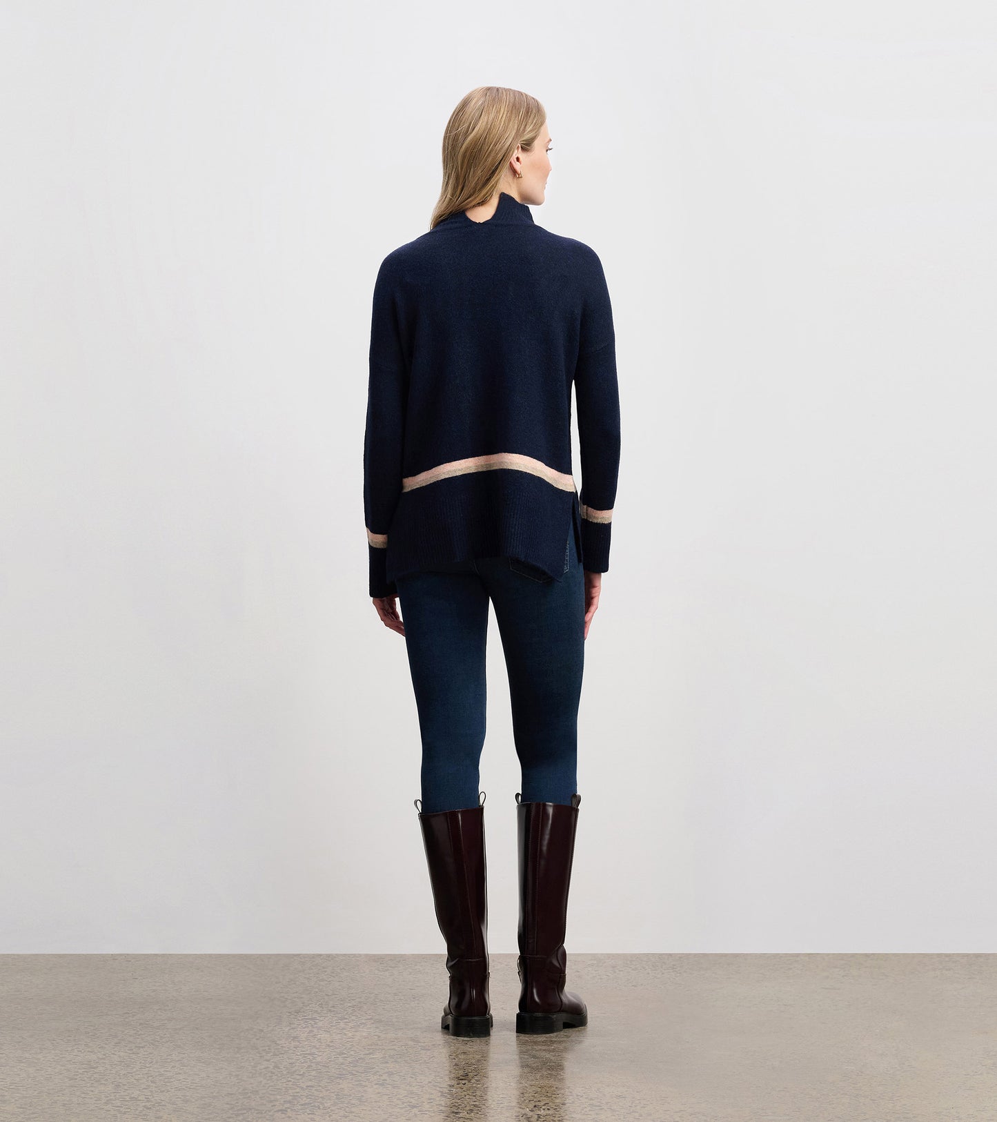 Navy mock neck sweater with a contrasting stripe at the hem, styled with fitted jeans and tall boots.