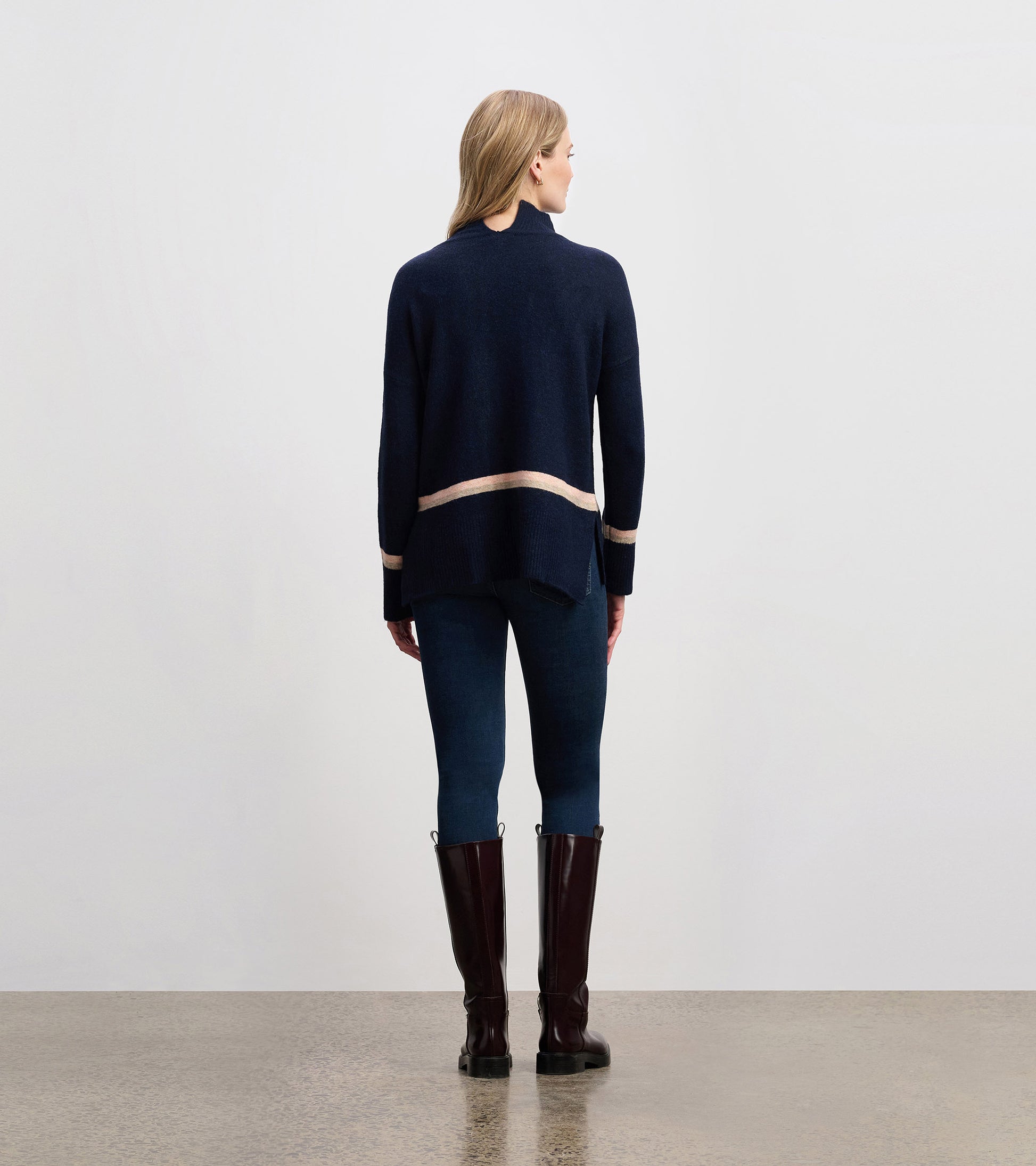 Navy mock neck sweater with a contrasting stripe at the hem, styled with fitted jeans and tall boots.