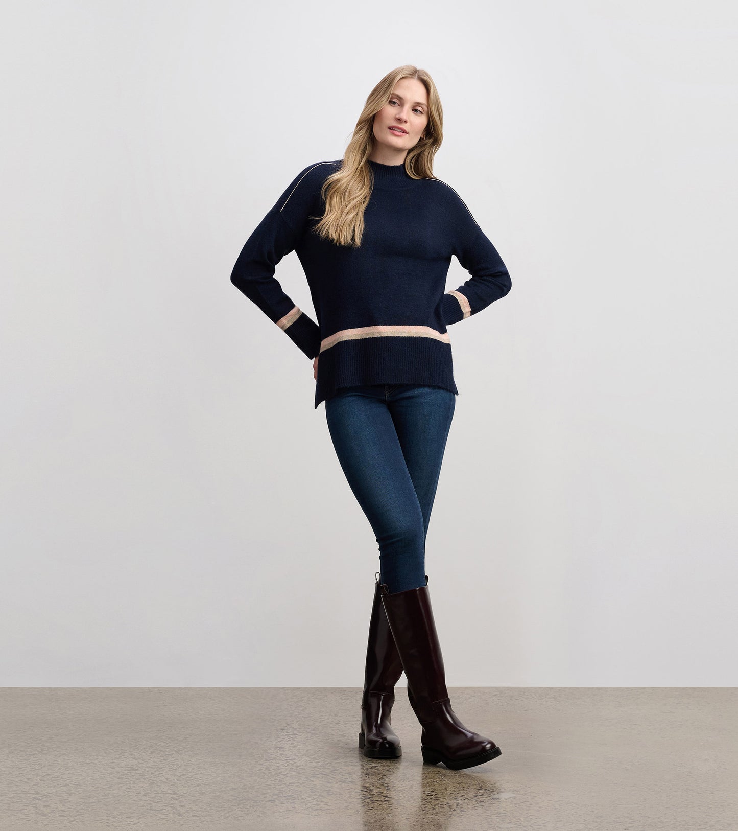 Navy mock neck sweater with light stripes, featuring a relaxed fit and ribbed hem, styled with jeans and tall boots.