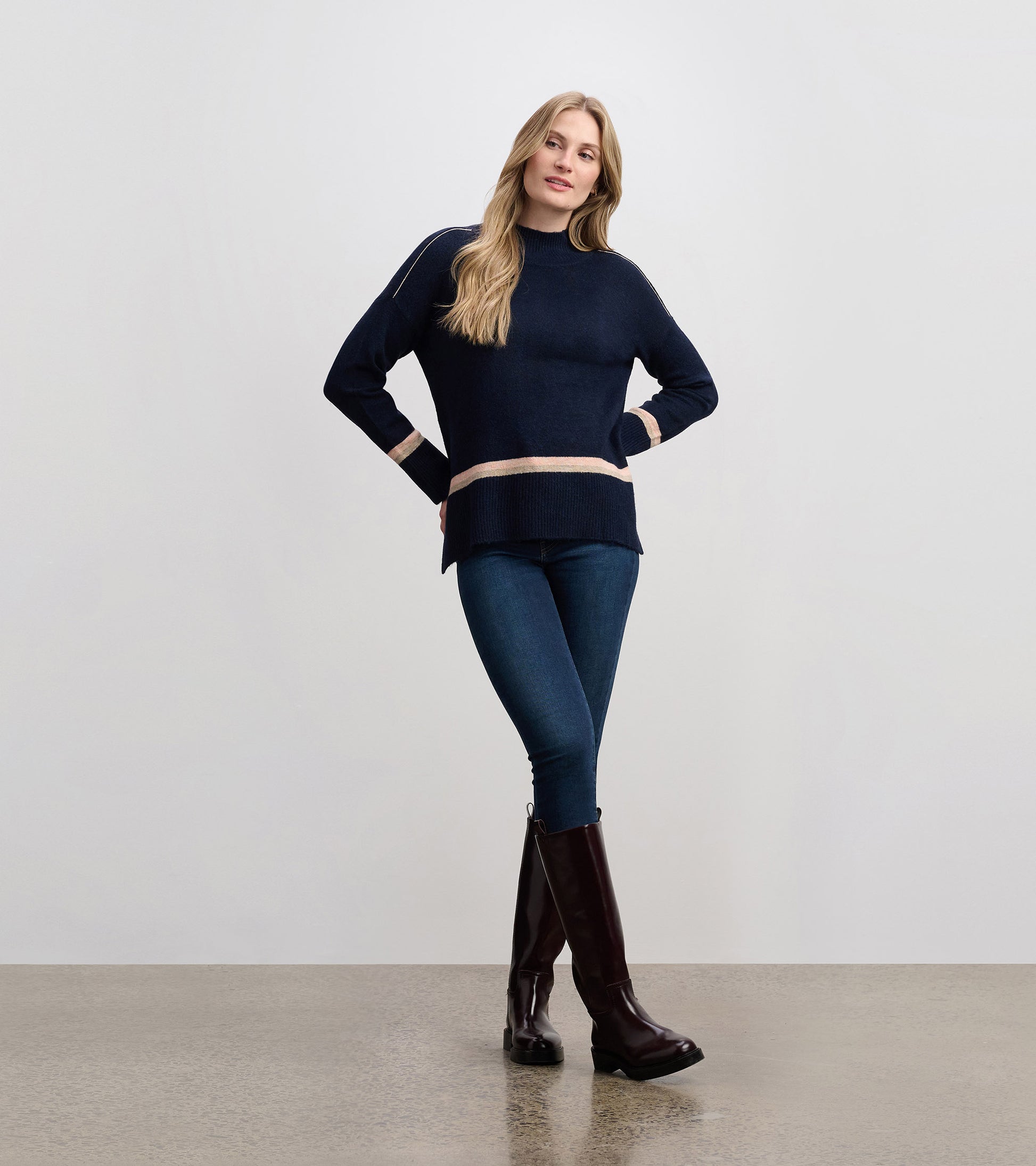 Navy mock neck sweater with light stripes, featuring a relaxed fit and ribbed hem, styled with jeans and tall boots.
