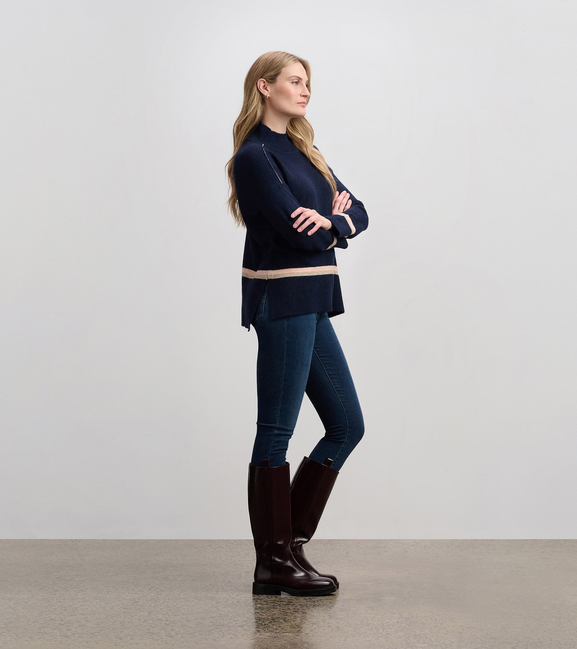 Navy mock neck sweater with a striped hem, paired with blue jeans and knee-high brown boots, shown from the side.