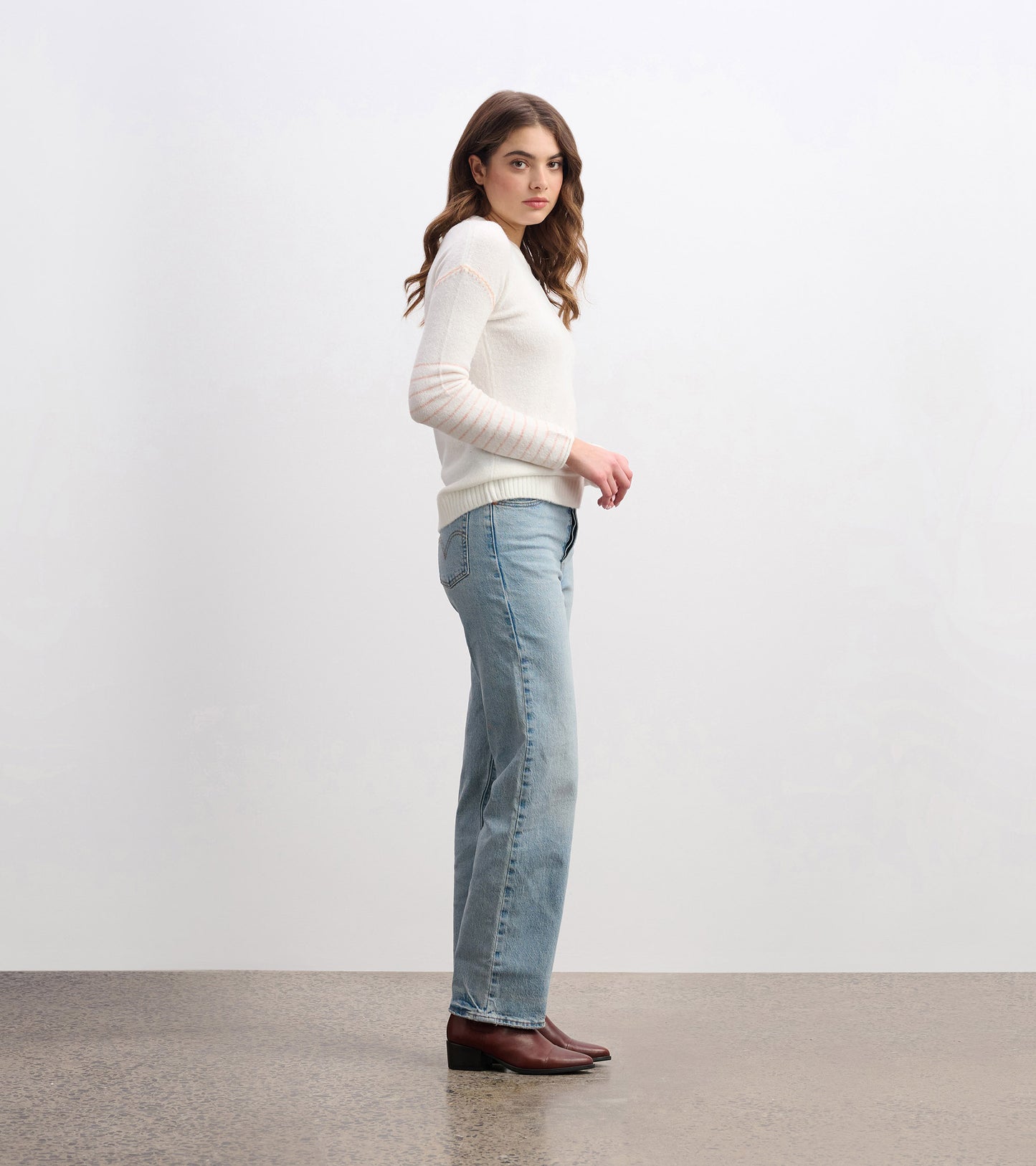 Cream sweater with long sleeves and striped detail, paired with light blue jeans, shown from the side.
