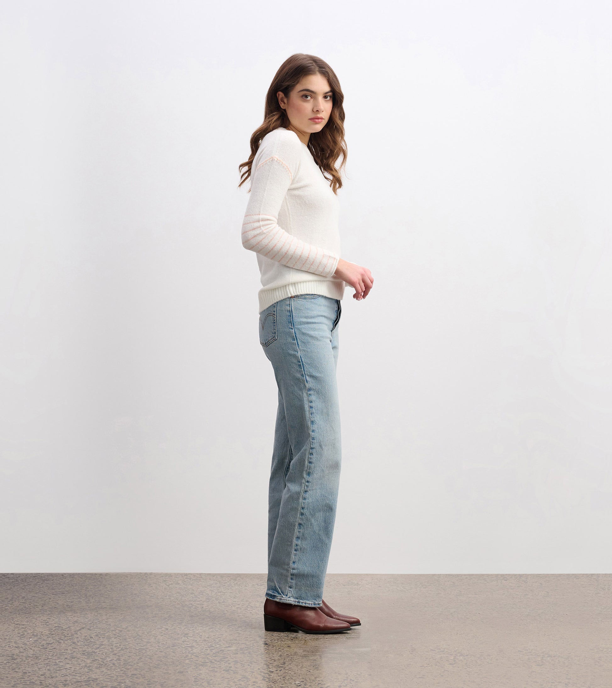 Cream sweater with long sleeves and striped detail, paired with light blue jeans, shown from the side.