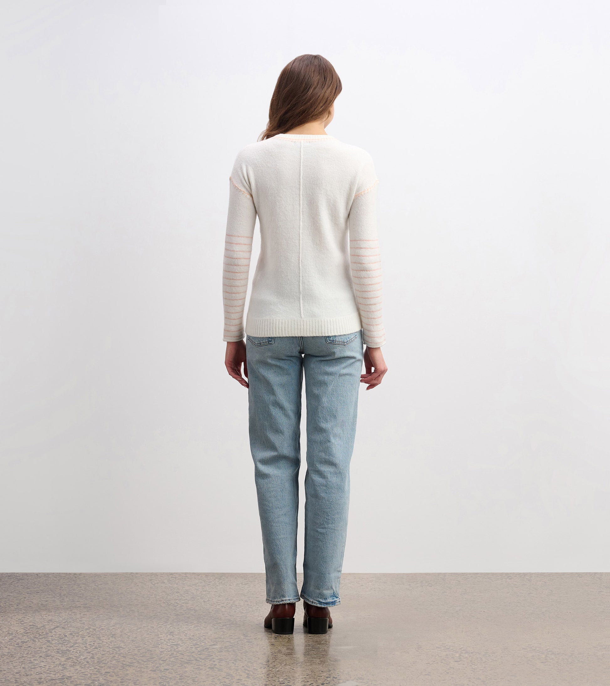 Cream sweater with striped sleeves, fitted shape, and ribbed hem, worn with light blue jeans, viewed from the back.