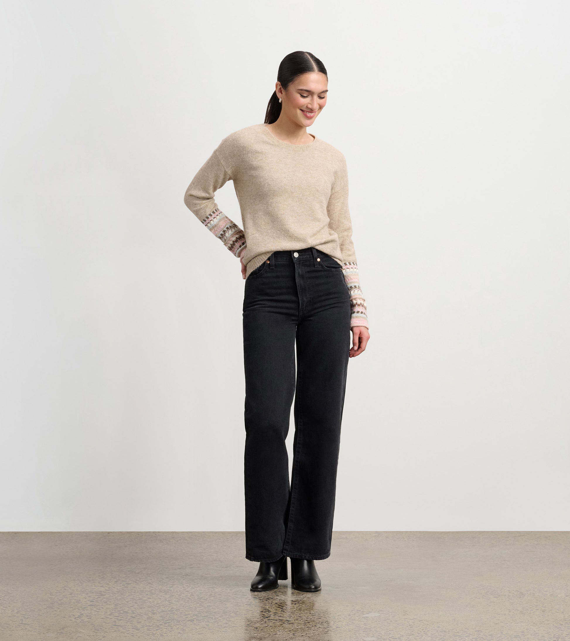 Oatmeal melange sweater with patterned cuffs, paired with black jeans, worn by a woman standing and smiling.