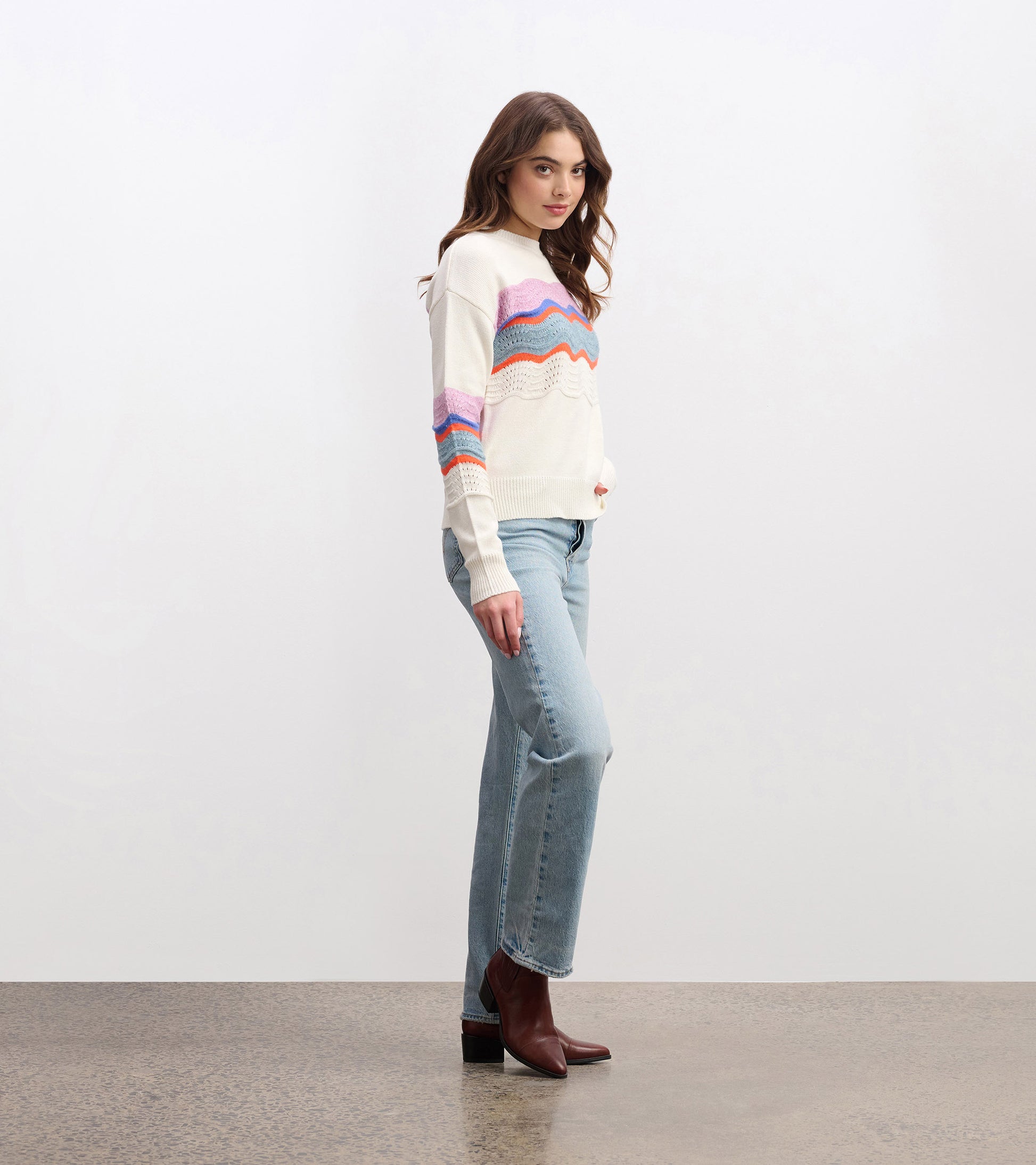 Lightweight cream sweater featuring a colorful wave pattern in pink, blue, and orange, styled with light jeans and boots.
