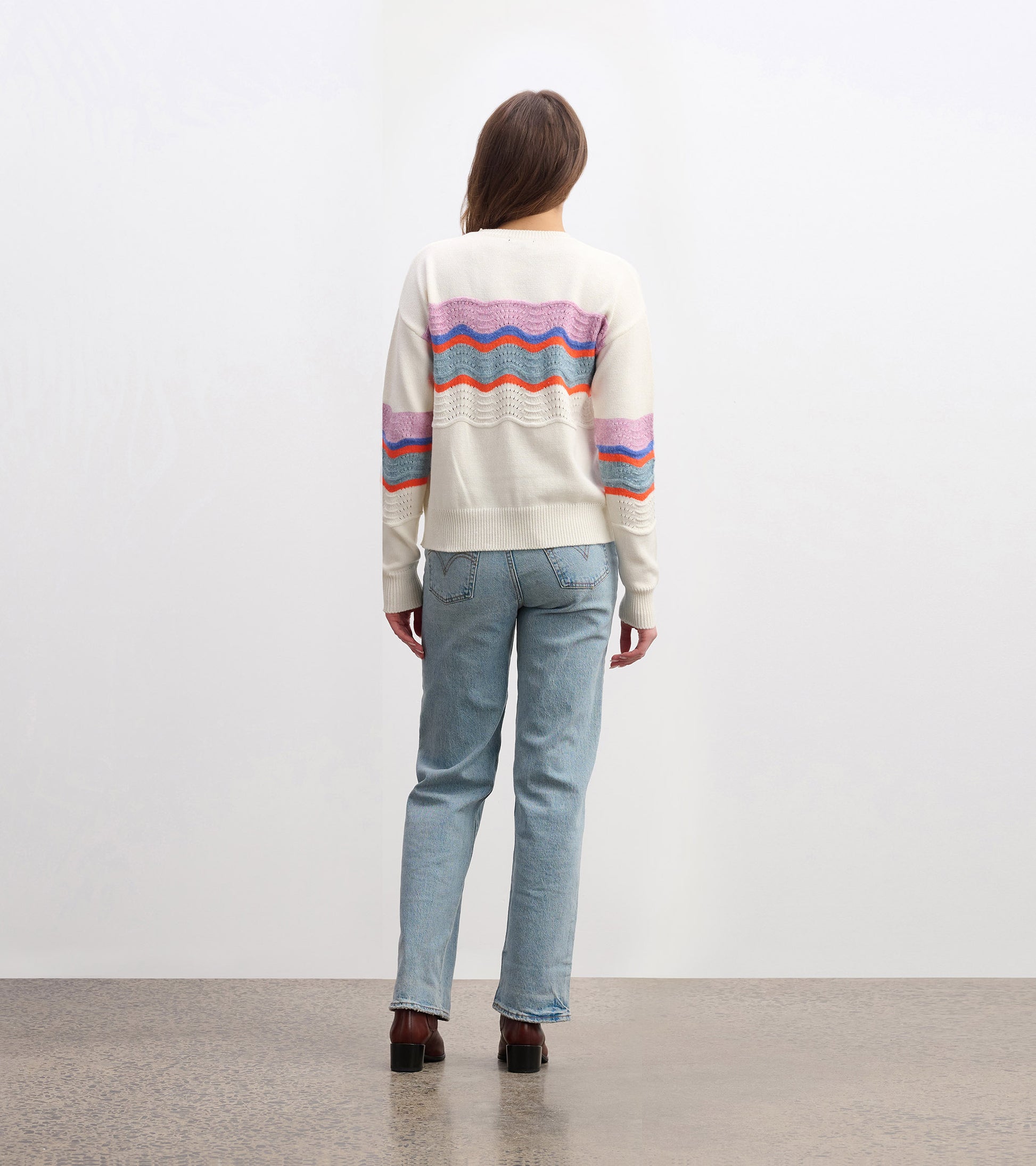 Back view of a cream sweater featuring colorful wave patterns in pink, orange, and blue, paired with light jeans.