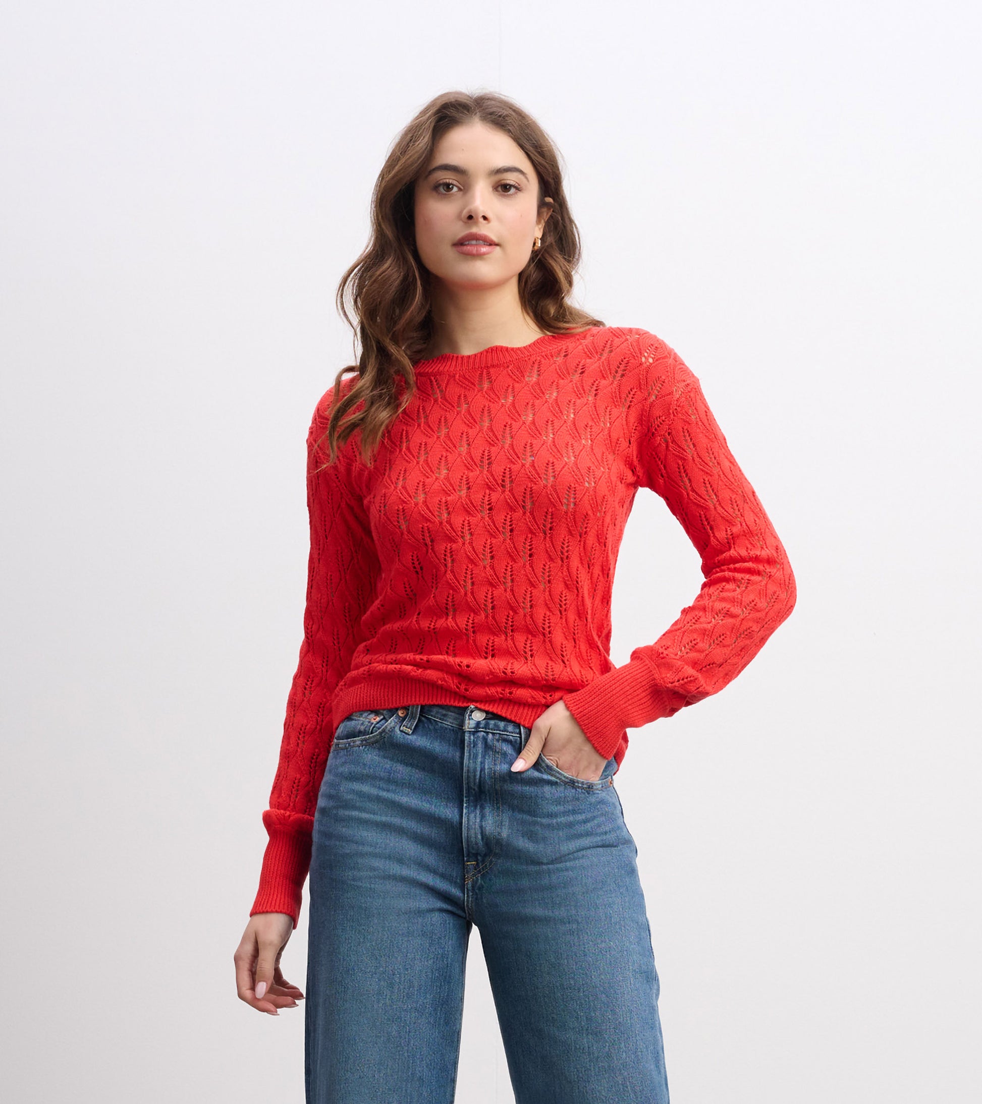 Ruby red knitted sweater with a textured pattern and long sleeves, styled with high-waisted jeans.