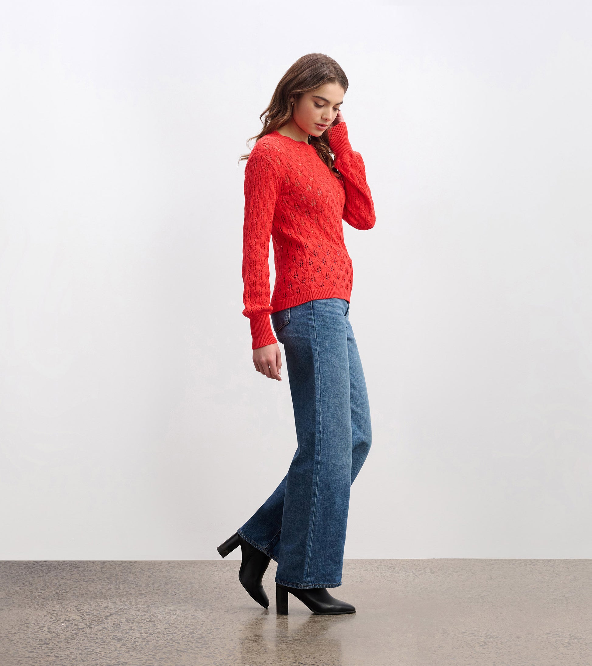 Ruby red knitted sweater with a textured pattern, paired with wide-leg jeans and black heels, shown from the side.