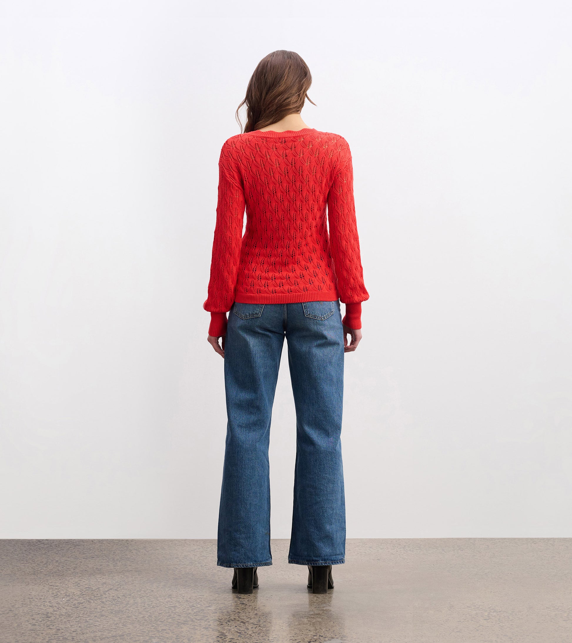 Ruby red sweater with a textured pattern, featuring long sleeves and a relaxed fit, worn with blue jeans.
