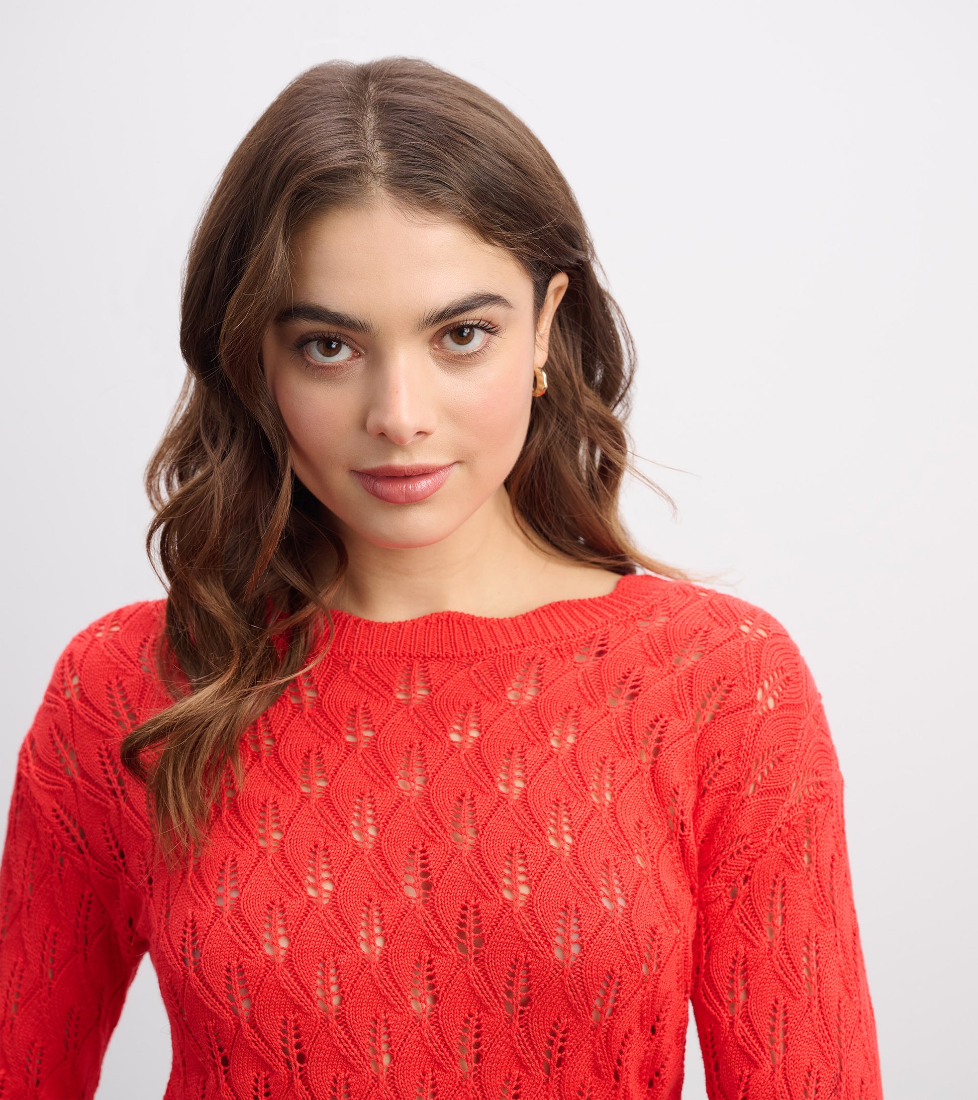 Ruby red knitted sweater featuring a leaf pattern and a round neckline, worn by a model with wavy hair.