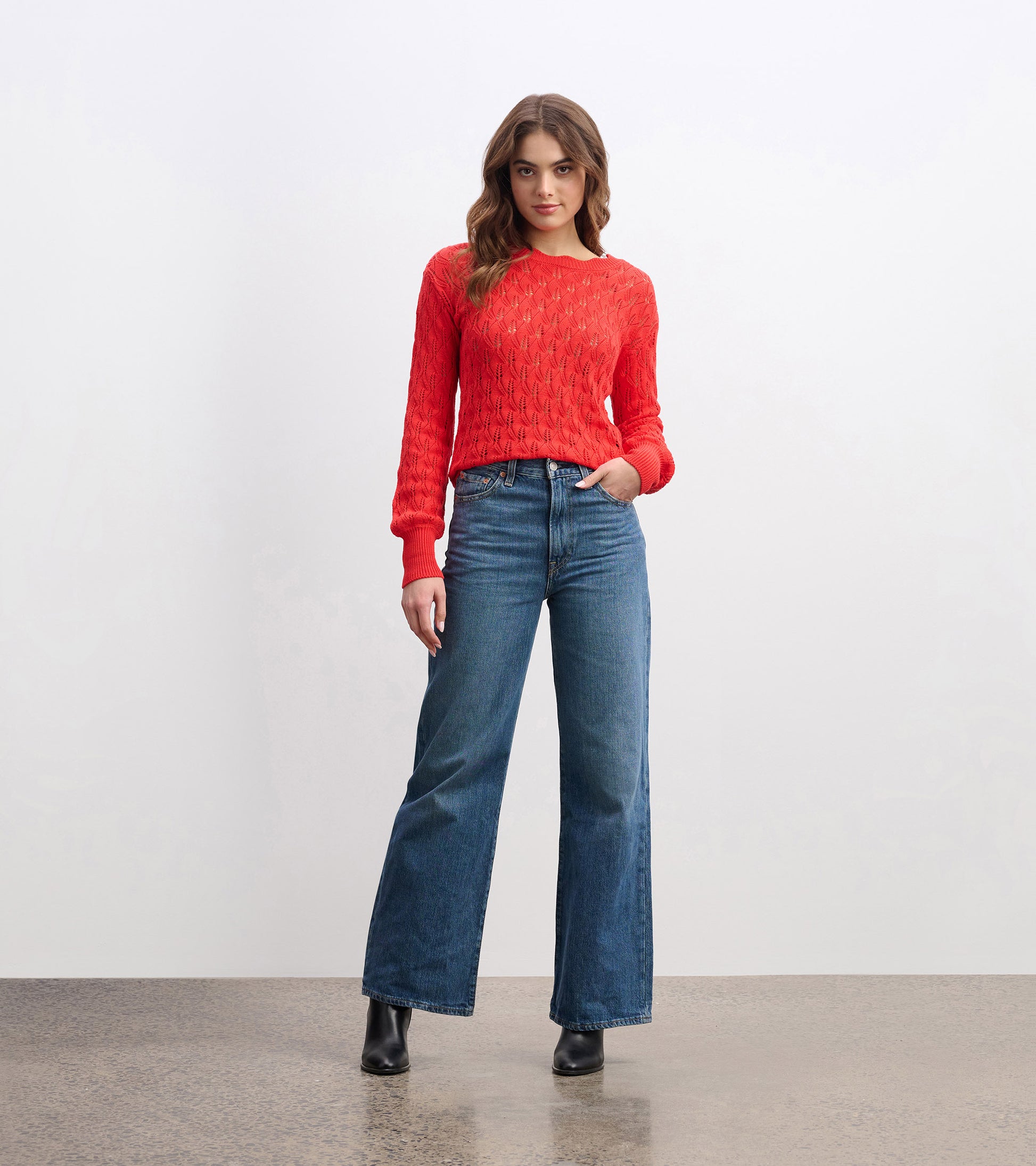Ruby red knitted sweater with a textured pattern, paired with high-waisted blue jeans and black ankle boots.