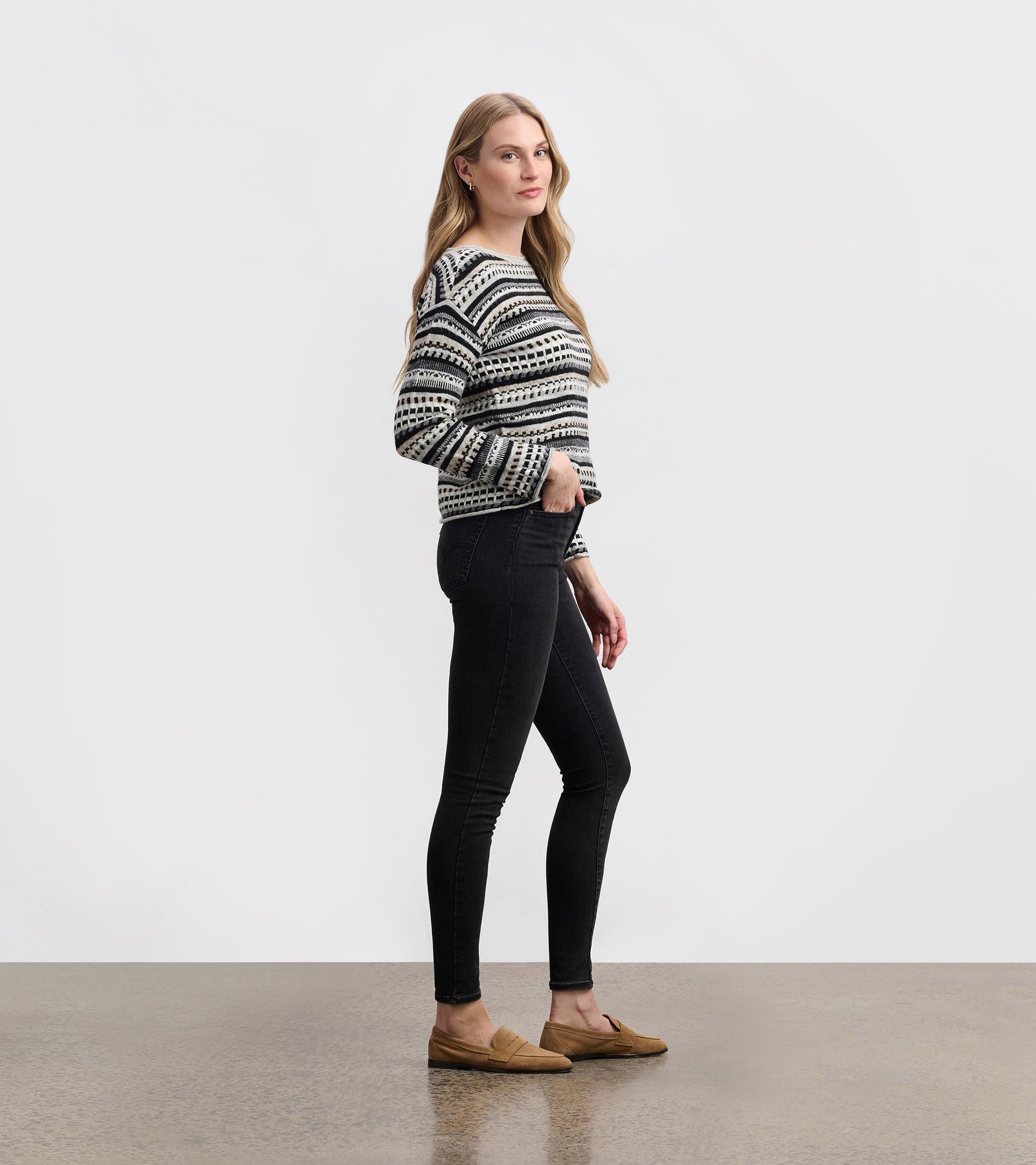 Stone grey sweater with a striped pattern, worn with black skinny jeans and loafers, shown from the side.