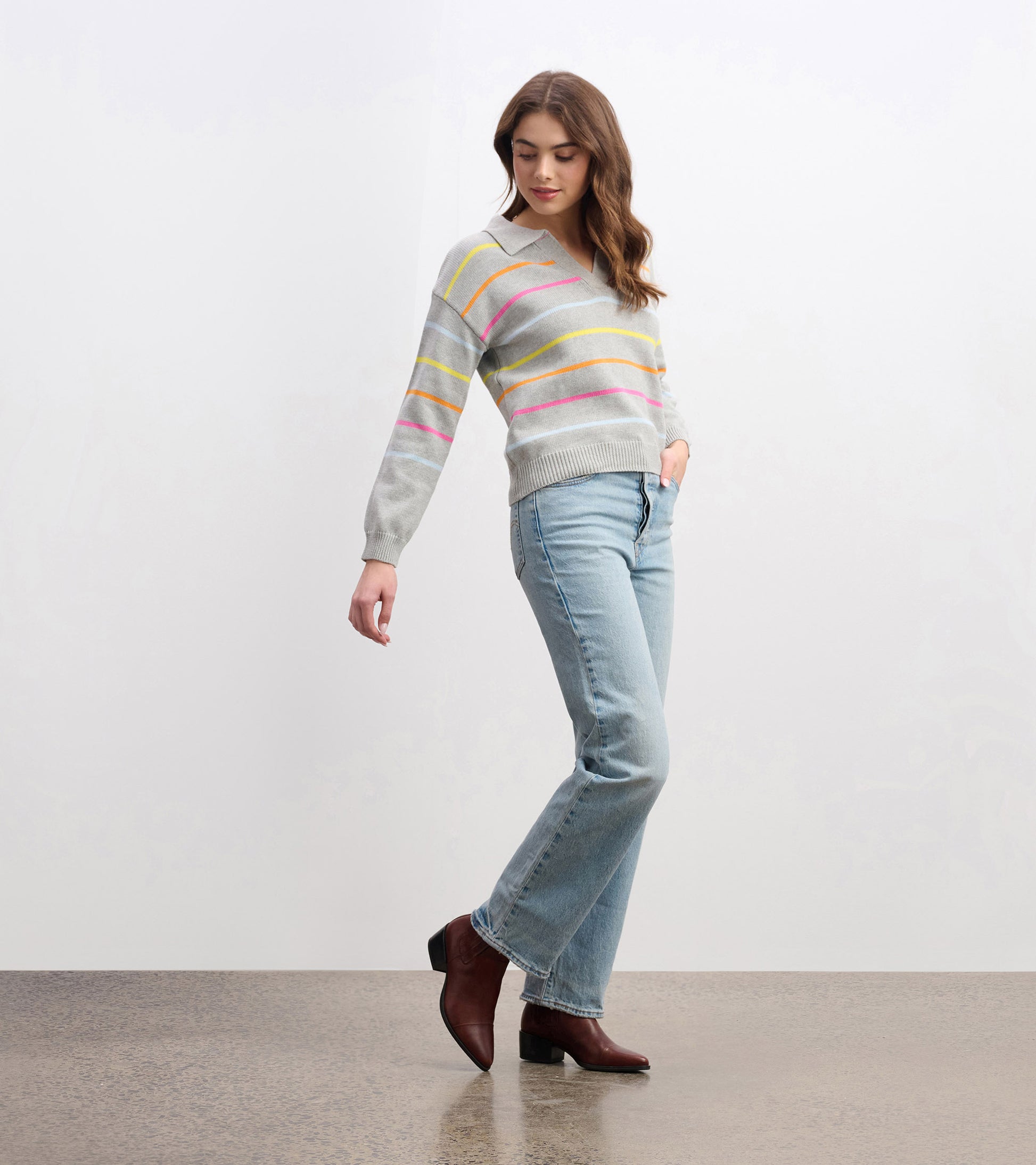 Gray sweater with colorful sorbet stripes, v-neck, and ribbed hem, styled with light blue jeans and brown heeled boots.