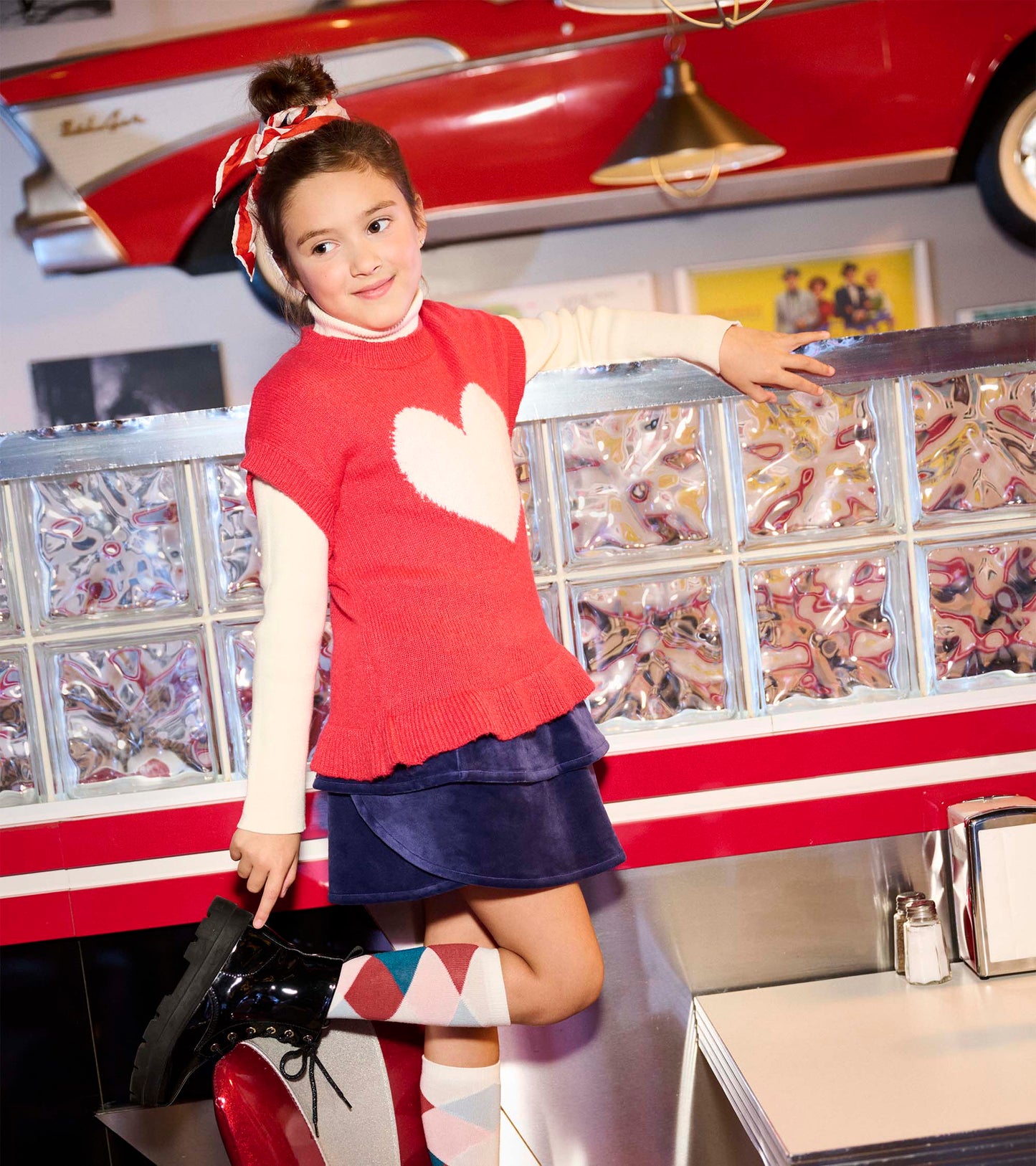 Red sweater vest with a white heart design, short sleeves, and a ruffled hem, styled with a navy skirt and patterned socks.