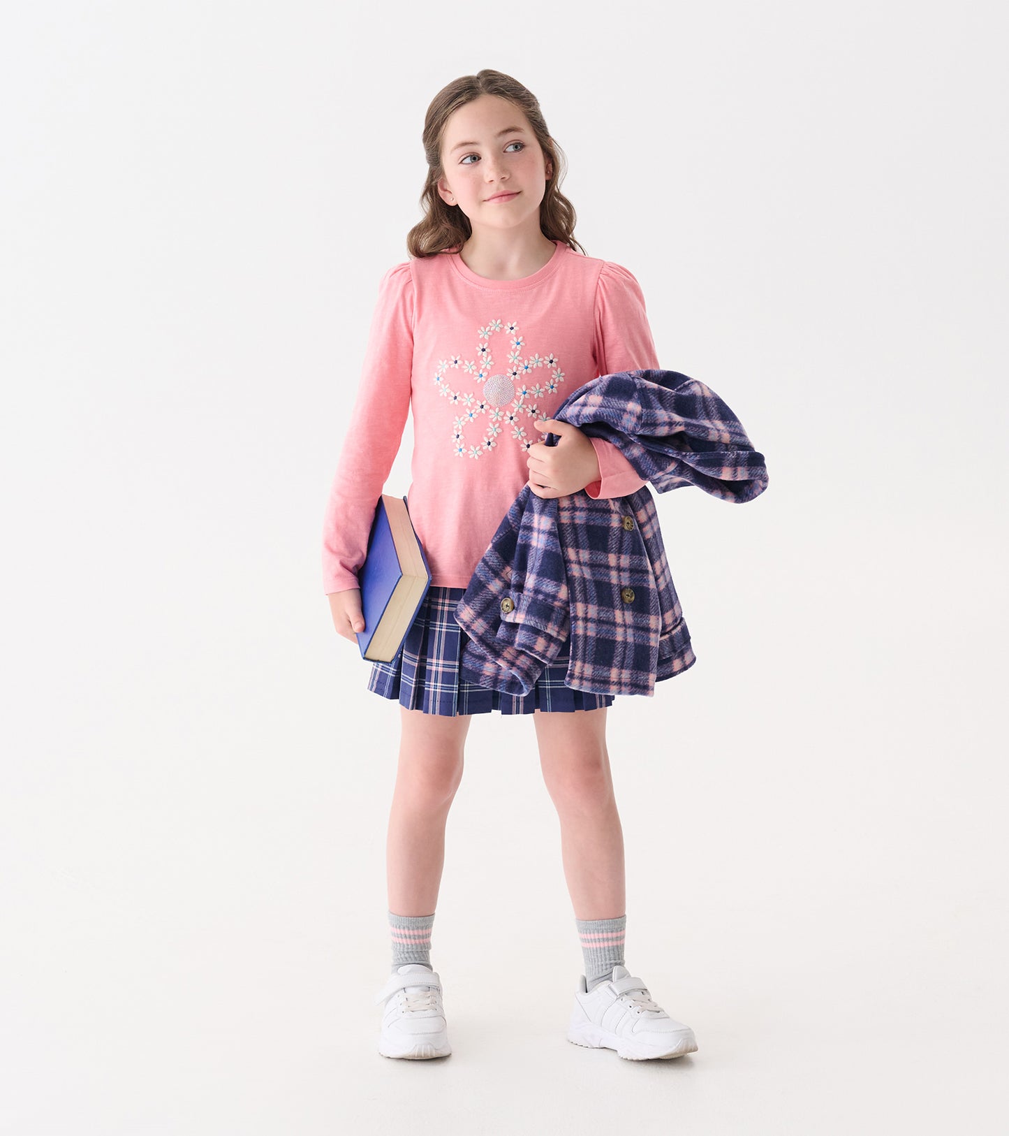 Pink puff sleeve tee with embroidered flower design, paired with a plaid skirt and holding a book and jacket.