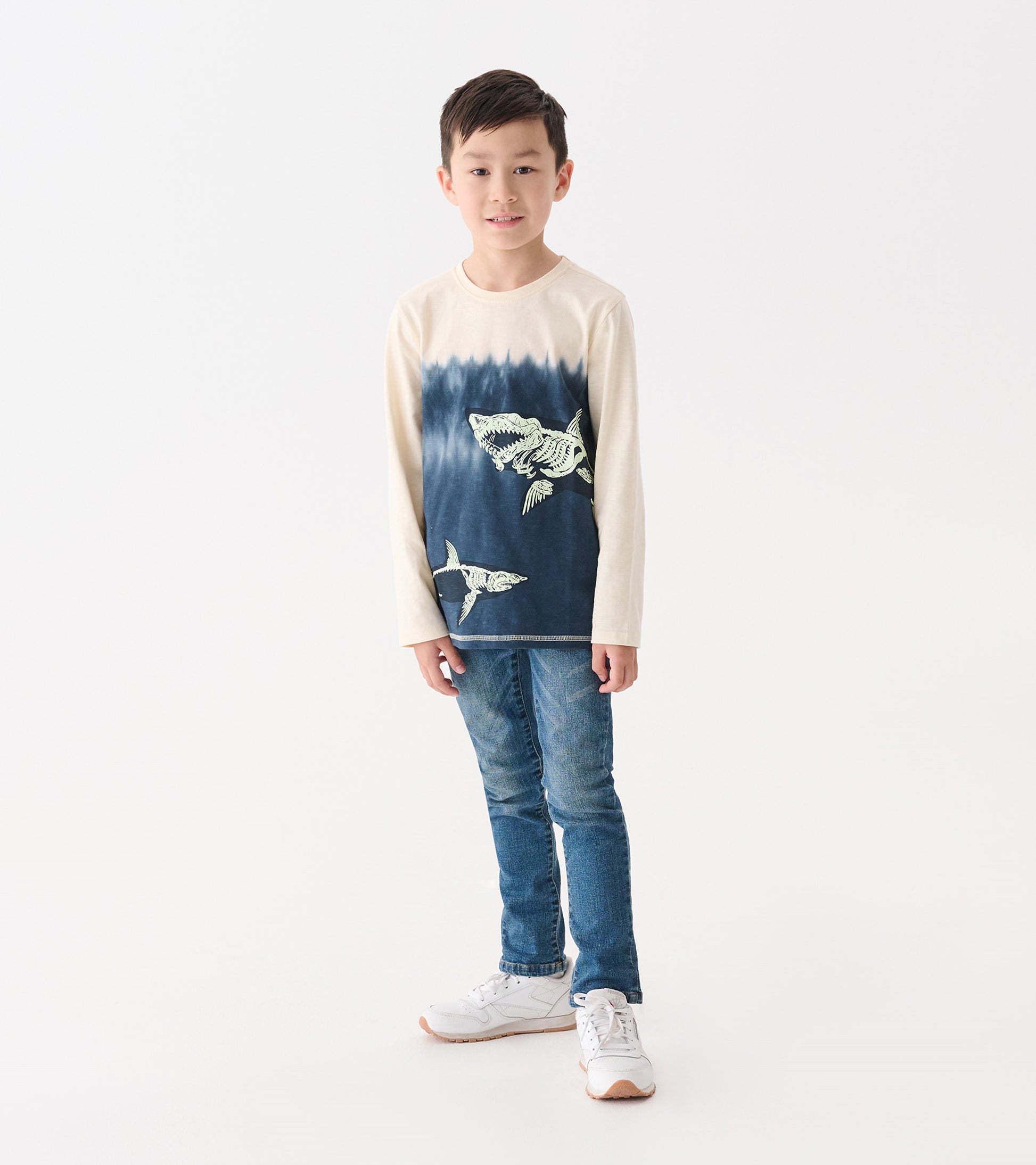 Long sleeve graphic tee featuring shark bone designs in blue and cream, worn by a boy with jeans and sneakers.