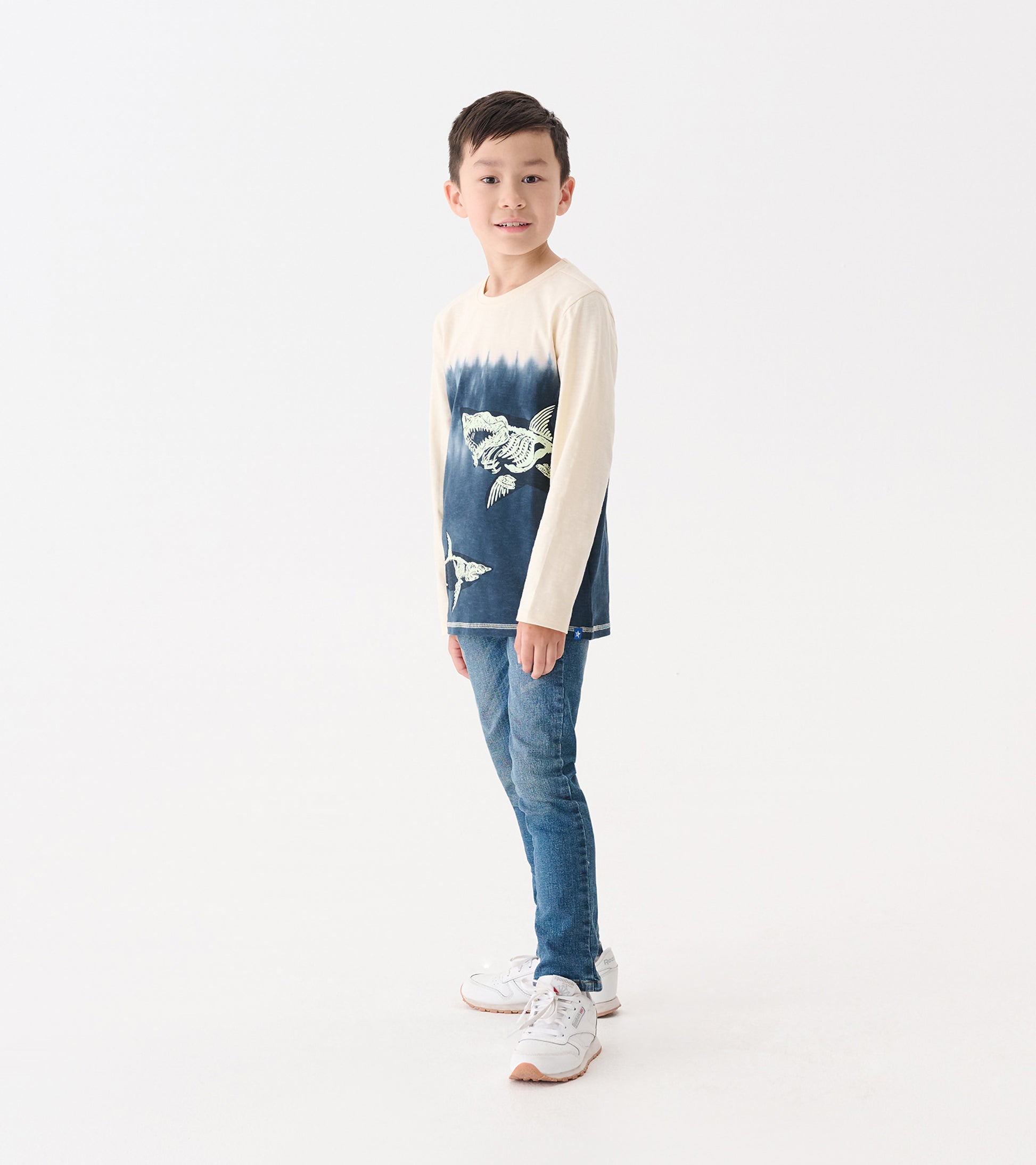 Long sleeve graphic tee featuring a shark design, cream and navy color gradient, worn by a boy with jeans.