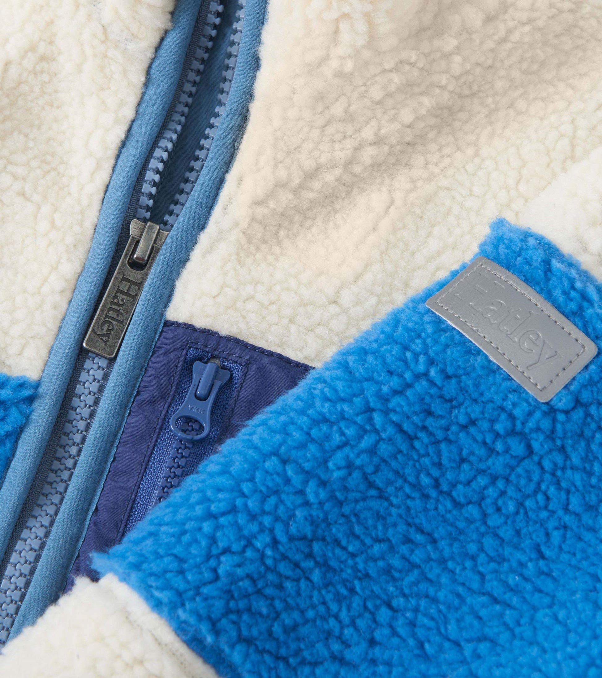 White faux sherpa zip-up jacket with blue accents and a textured finish, featuring a front zipper and logo patch.
