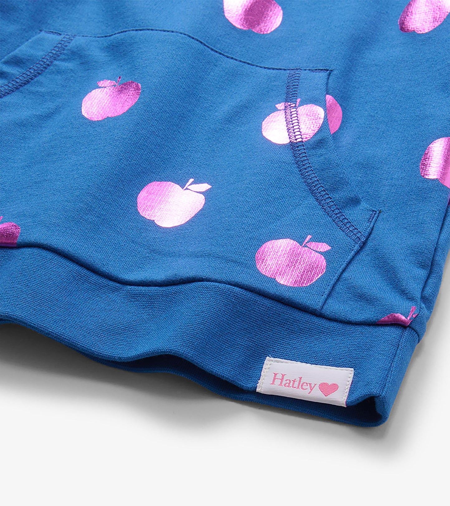 Close-up of blue pullover kangaroo pocket with pink foil apple print and visible Hatley hem label