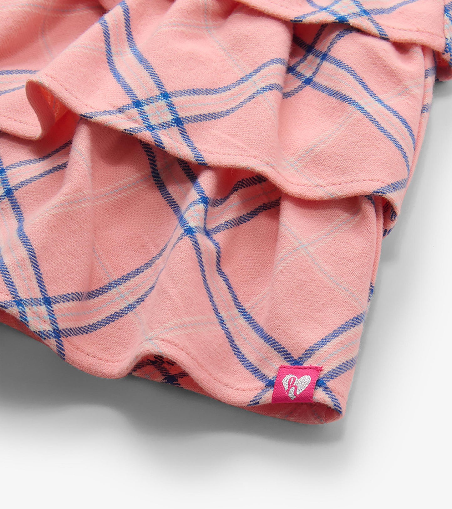 Close-up of the skirt hem with pink plaid ruffles and a small heart tag