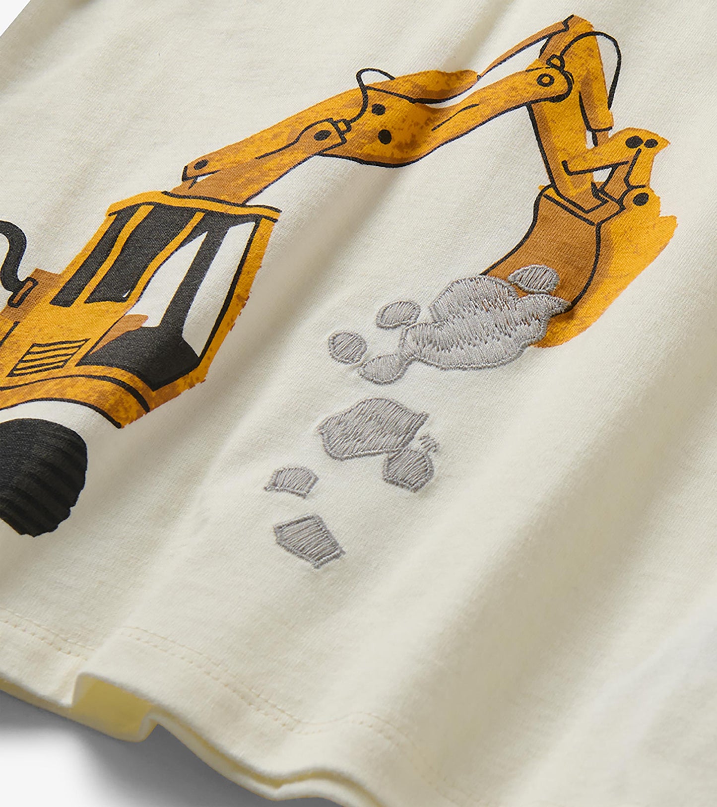 Close-up of yellow digger graphic with gray embroidered rocks on cream T-shirt