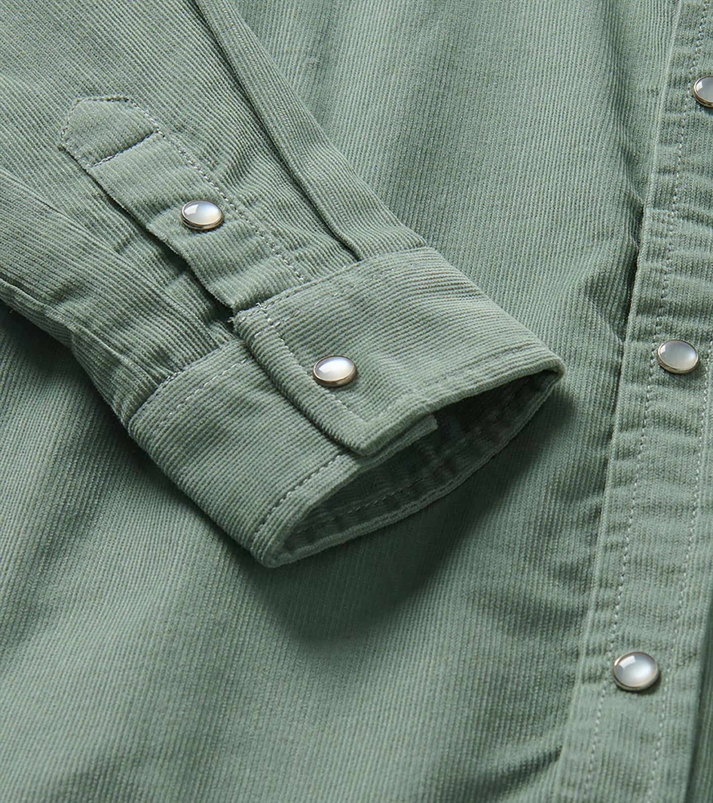 Close-up of green shirt cuff and sleeve tab with pearl snap buttons and fine vertical texture