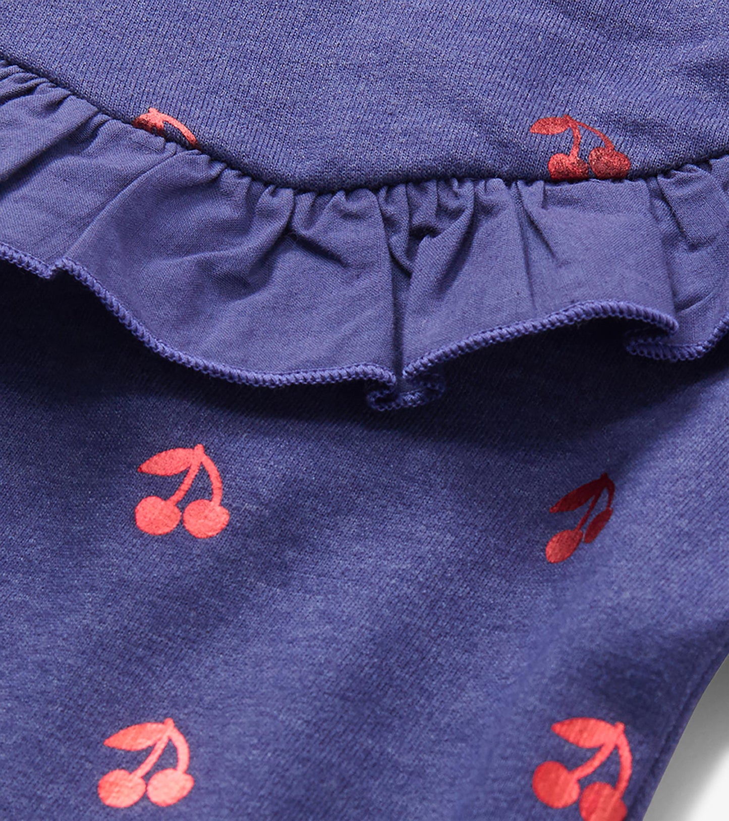 Close-up of blue dress ruffle detail with red cherry print