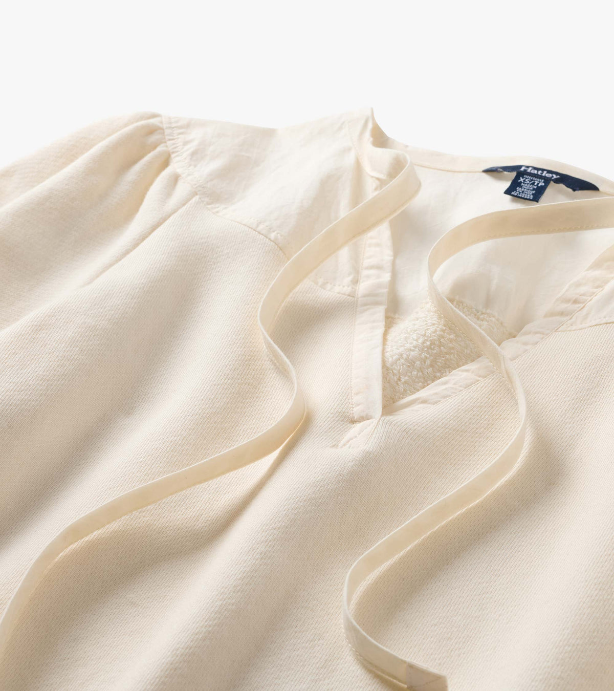 Close-up of cream top with tie neckline, gathered shoulders, and mixed panel detailing