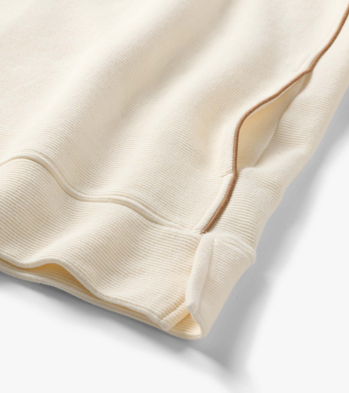 Close-up of cream quarter-zip top with fine ribbed texture and tan piping at the side seam