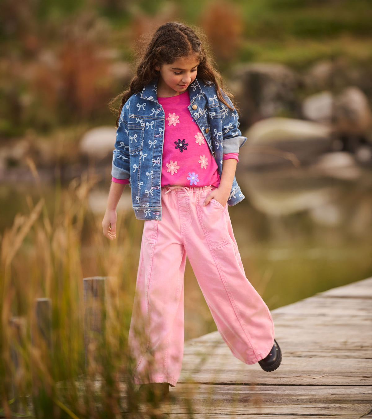 Girl modeling a blue bow-print denim jacket with rolled cuffs and pink pants