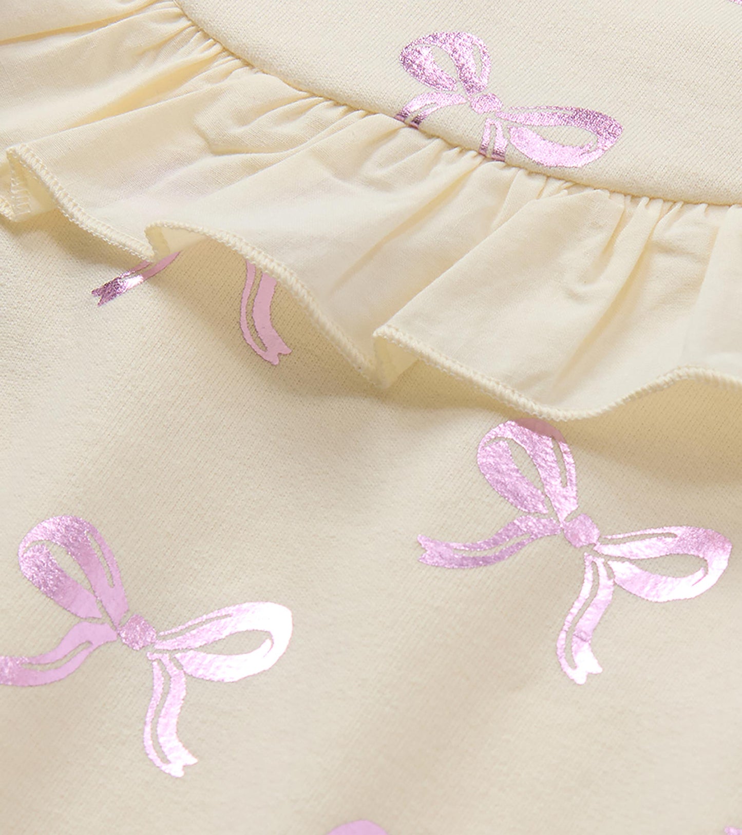 Close-up of cream dress ruffle trim with pink foil bow print
