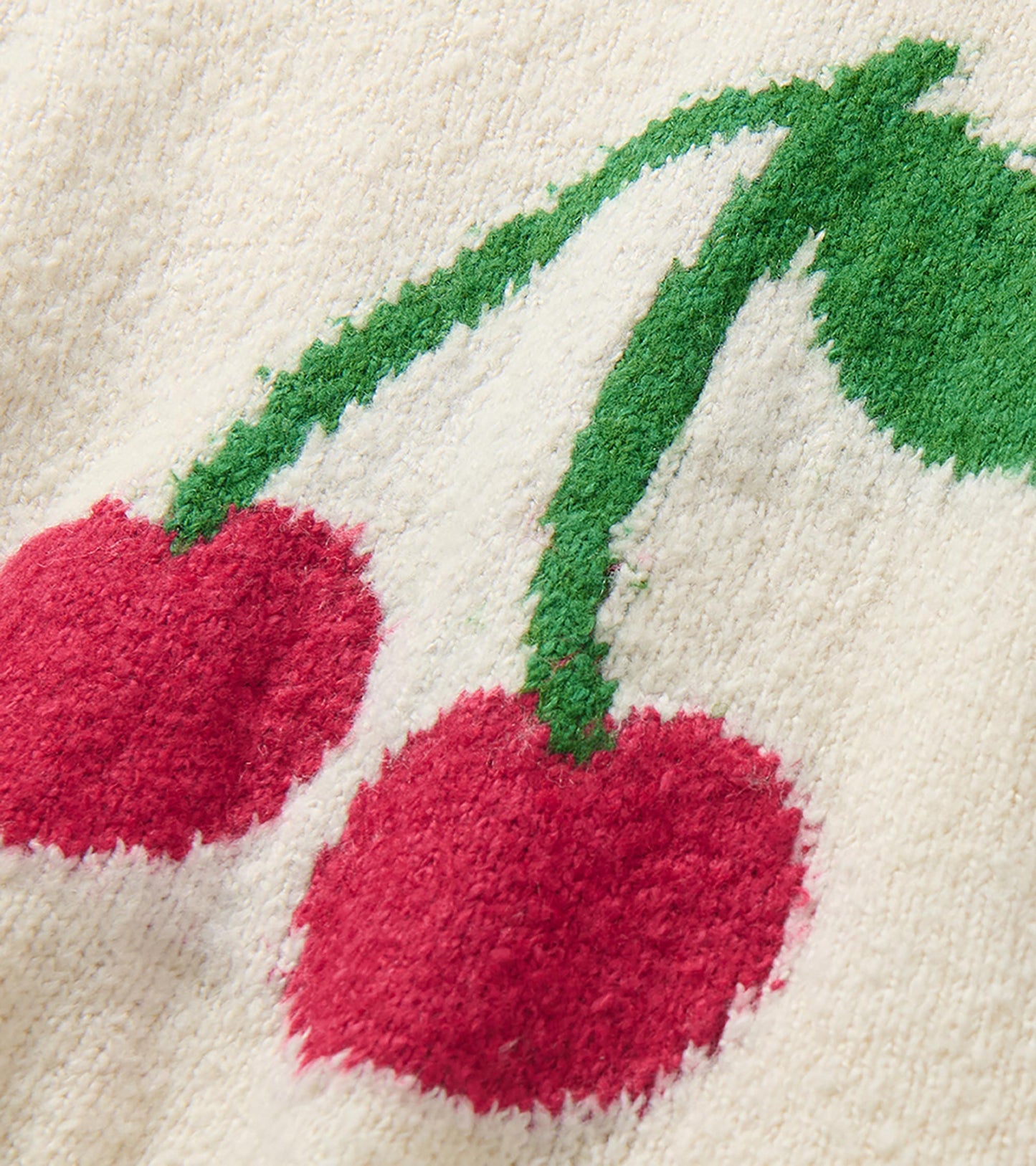 Close-up of red cherry and green leaf motif on cream knit sweater