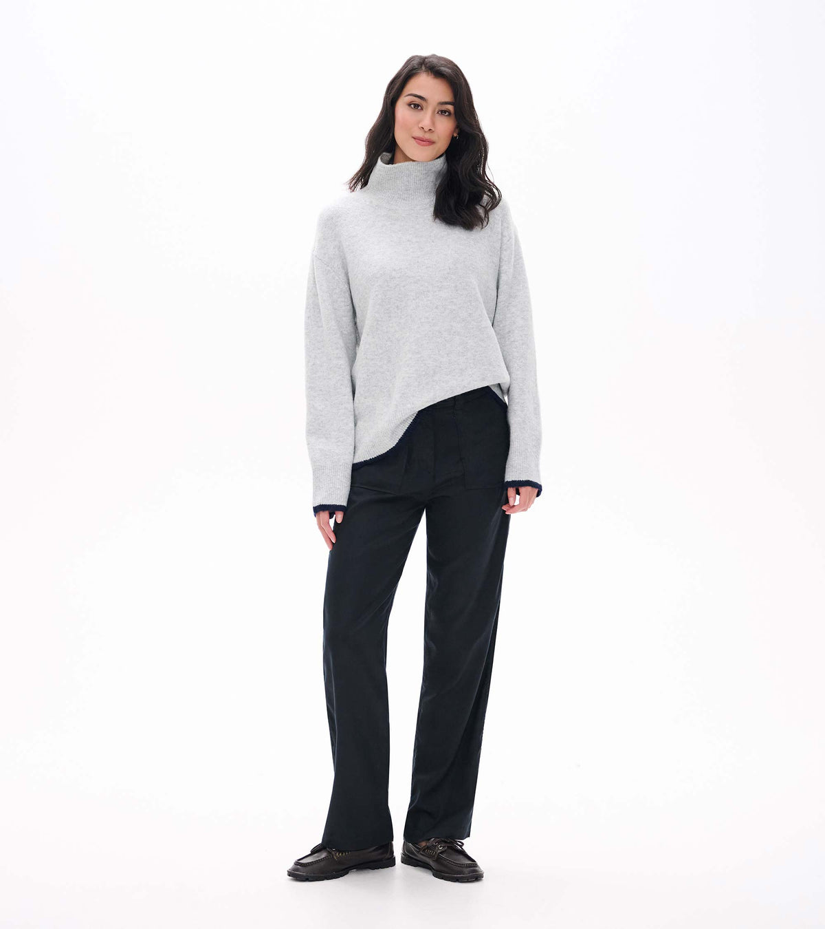 Front angled view of athletic grey mock neck sweater with asymmetric drape and navy trim at cuffs and hem