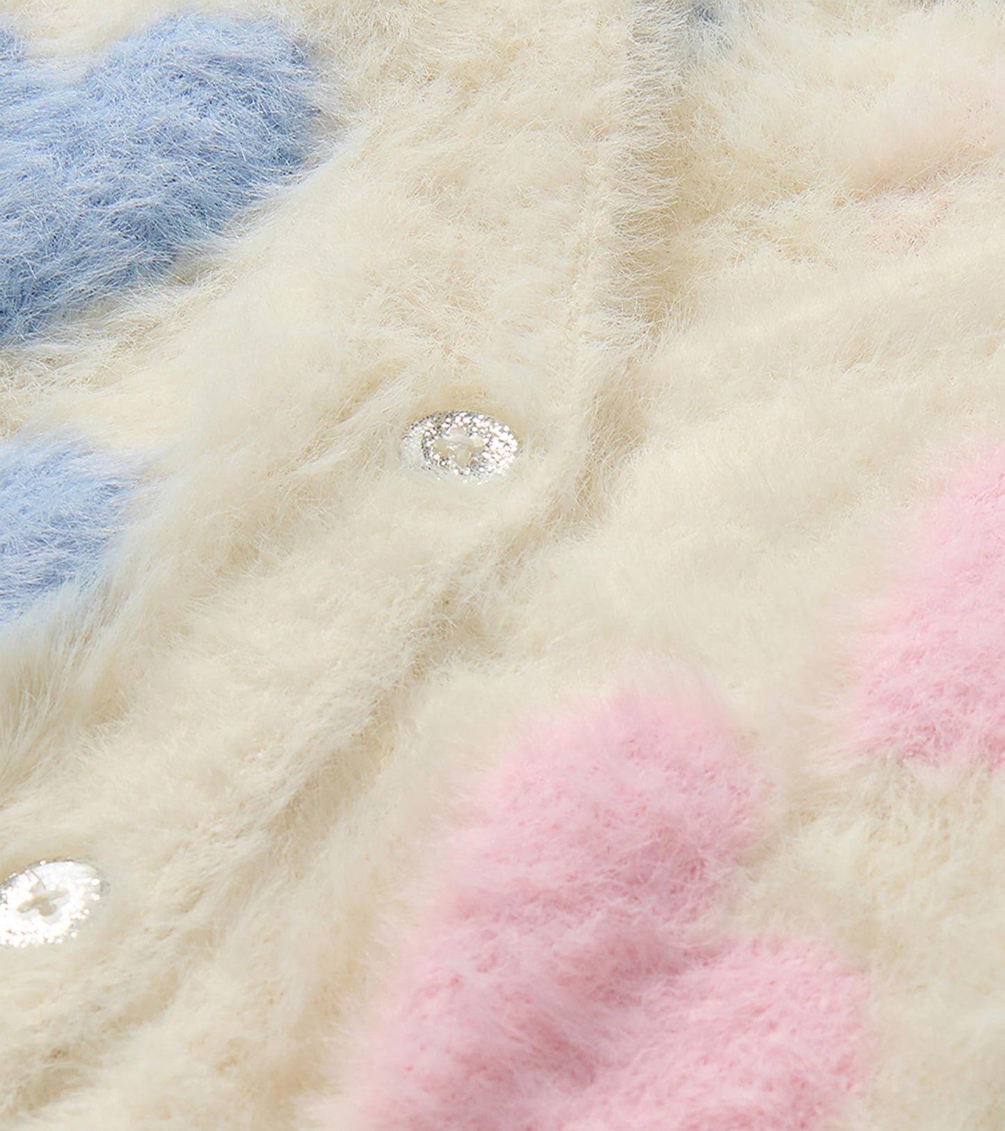Close-up of cream fuzzy cardigan with pink and blue hearts and a glitter button detail