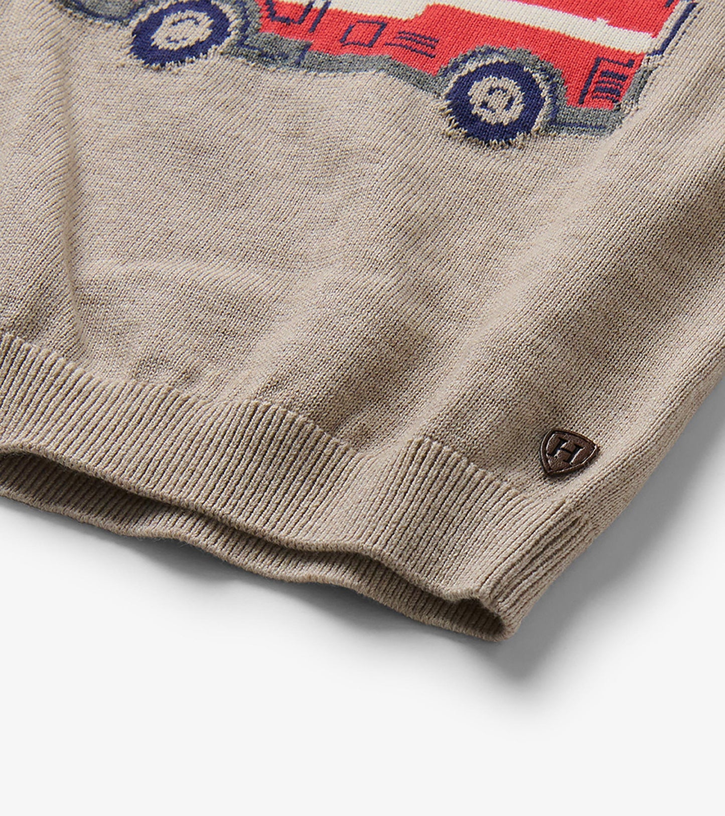 Close-up of oatmeal marl sweater hem with partial firetruck graphic and small Hatley badge