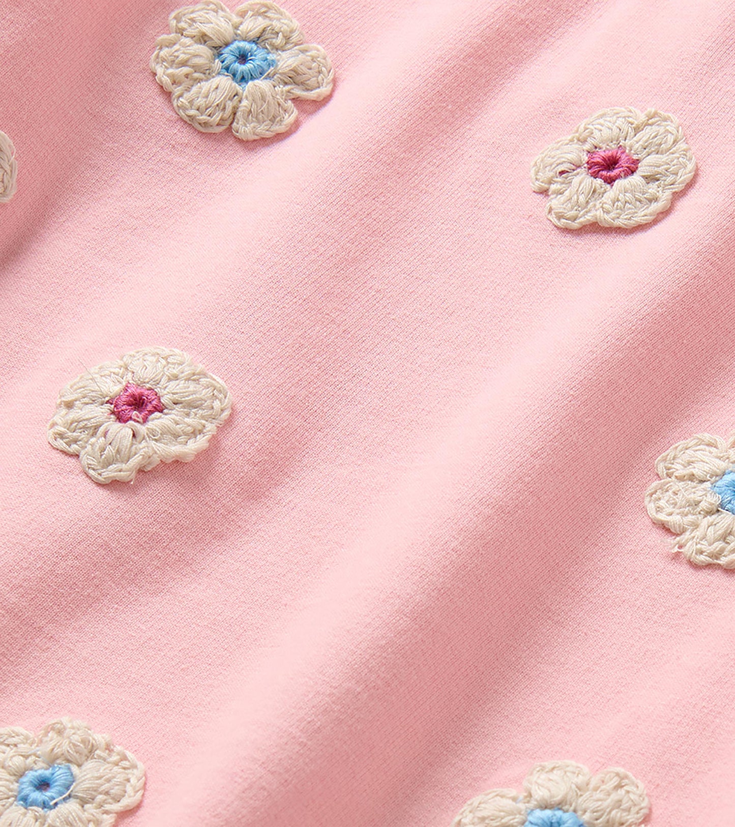 Close-up of cream crochet-style flower appliques with blue and pink centers on pink dress