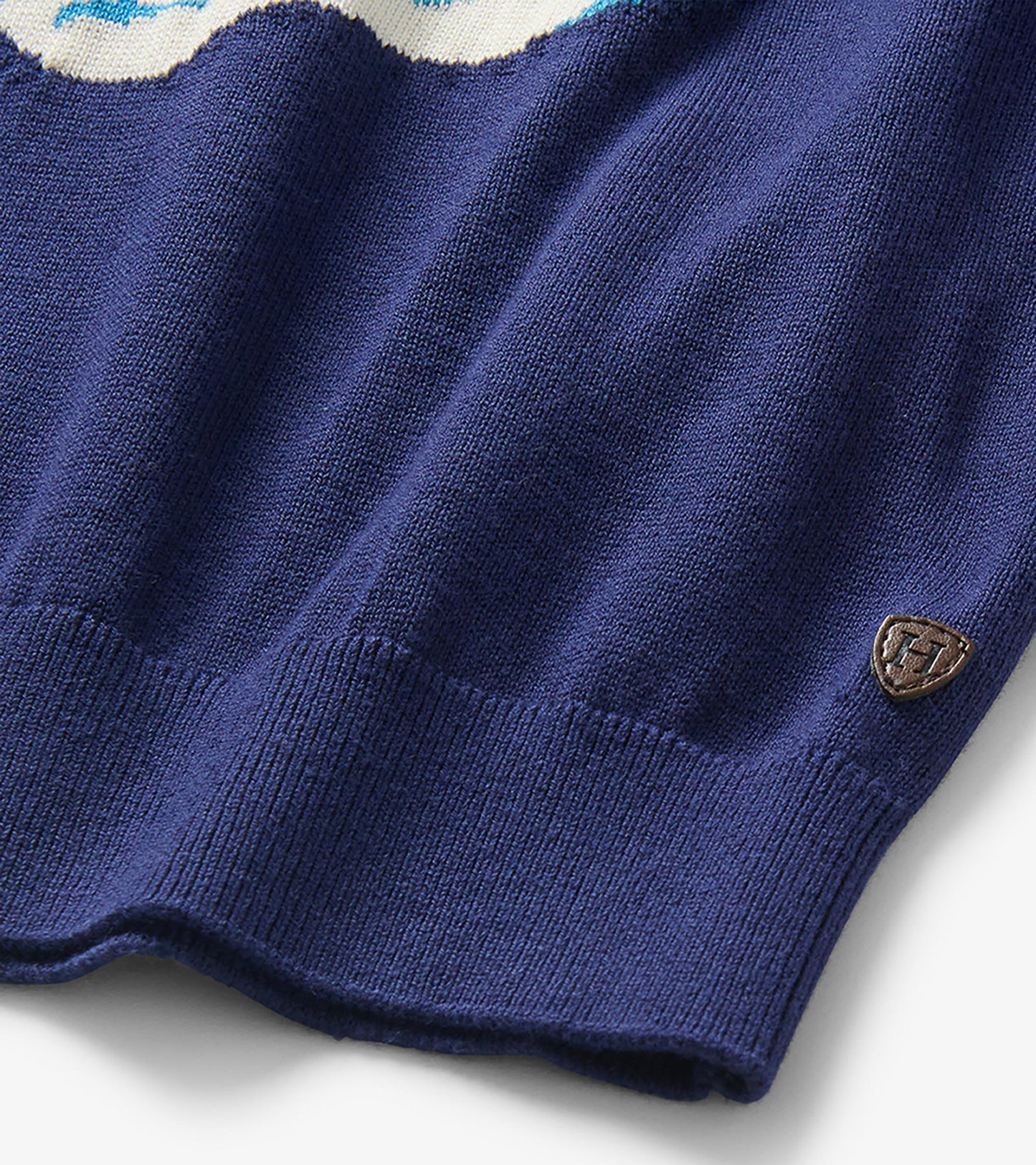 Close-up of the navy sweater hem and knit texture with a small shield-shaped logo patch