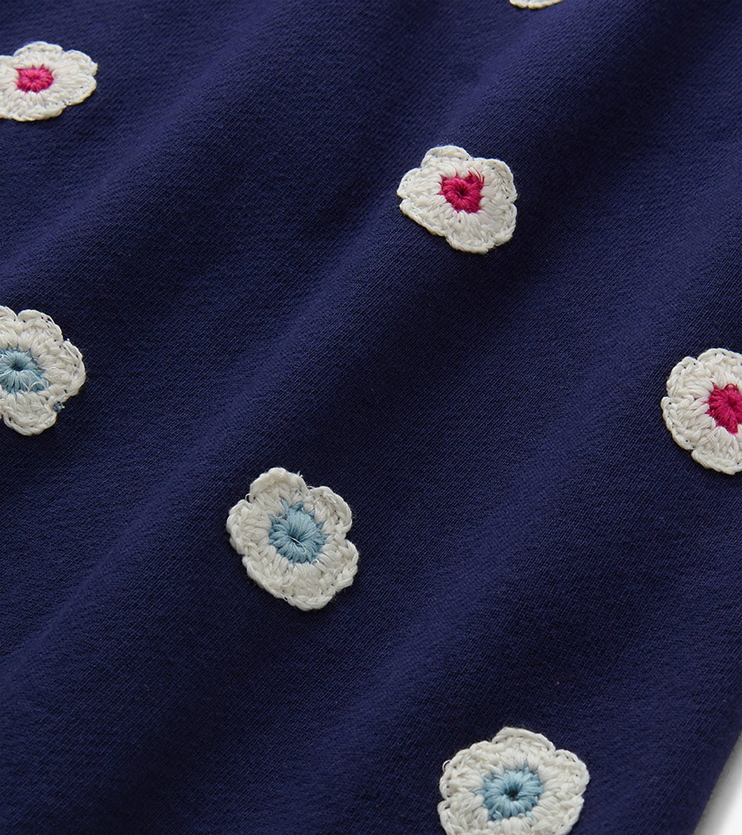 Close-up of patriot blue dress fabric with scattered cream crochet flowers in pink and light blue.
