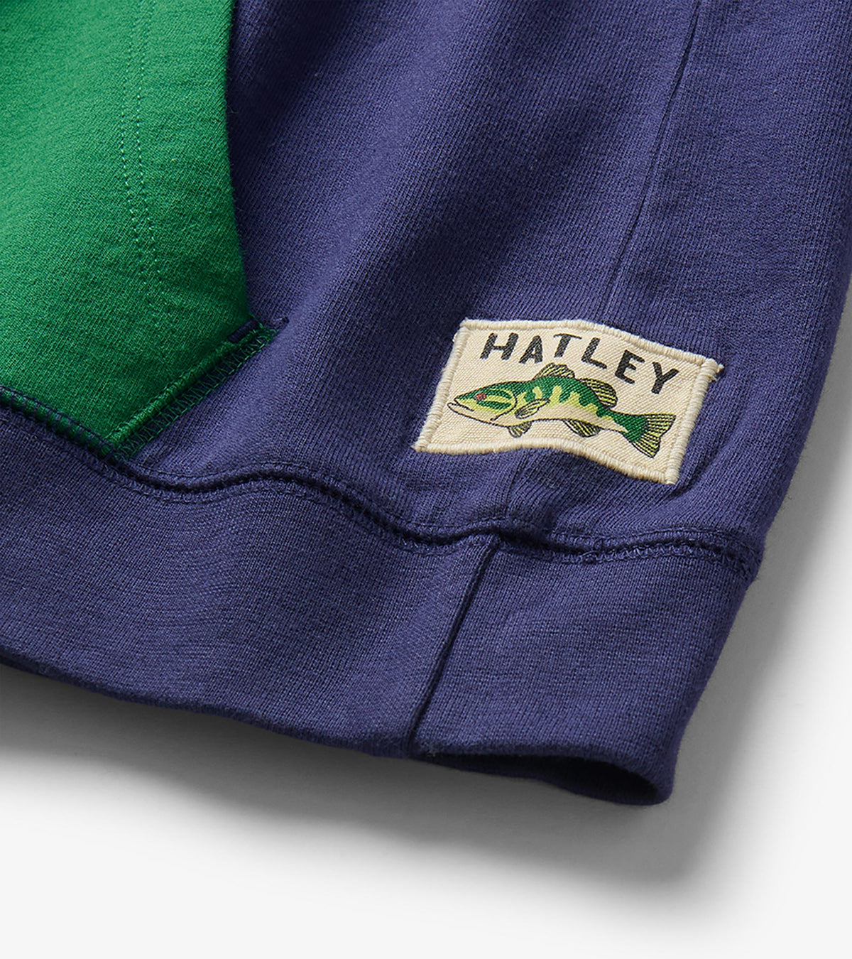 Close-up of Hatley fish logo label at the hem beside the green kangaroo pocket