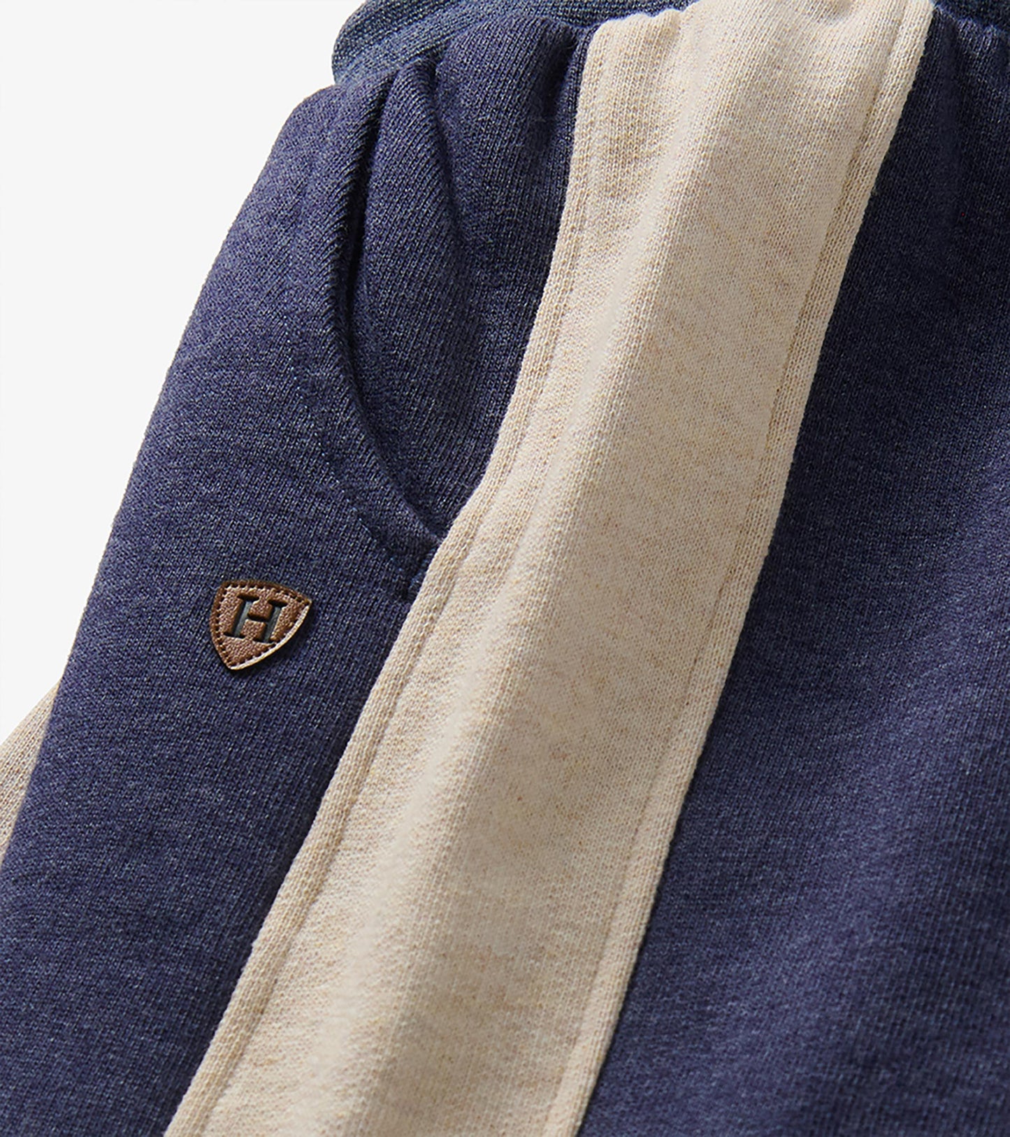 Close-up of blue melange track pants with oatmeal side panel, pocket seam, and small H patch