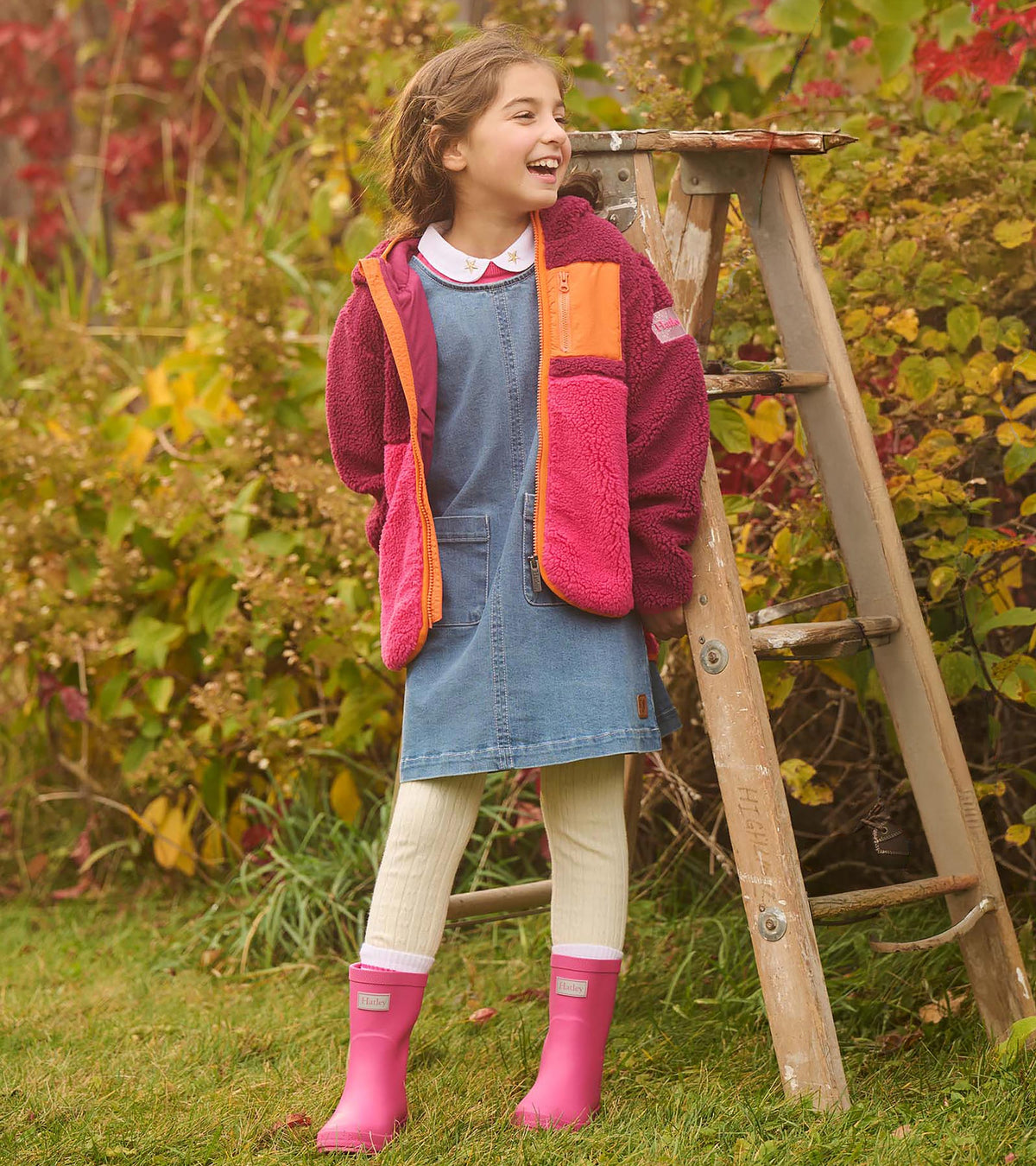 Girl outdoors wearing bright pink rain boots with a denim dress and color-block fleece jacket