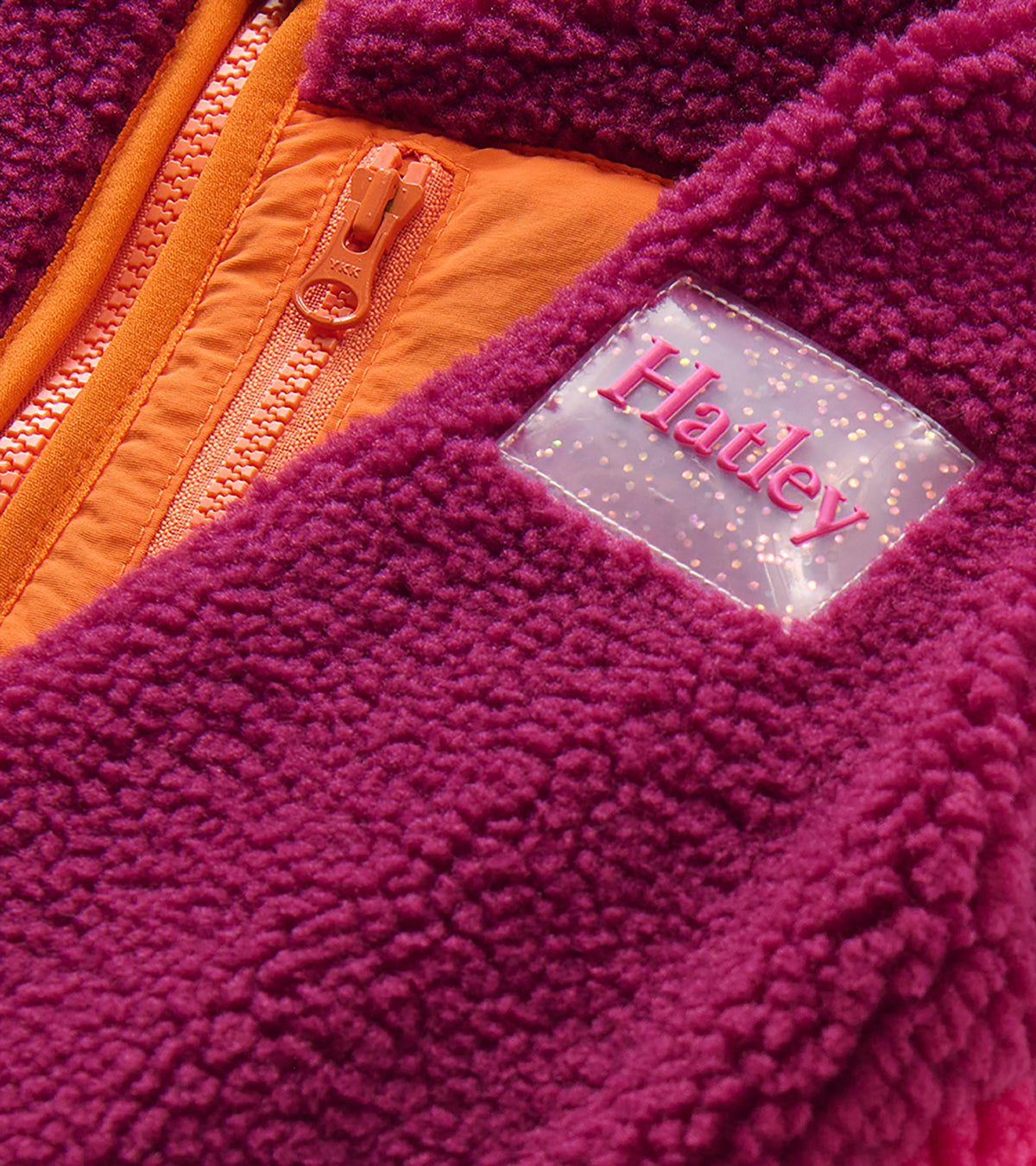 Close-up of raspberry sherpa jacket with orange zip chest pocket and clear Hatley sleeve patch