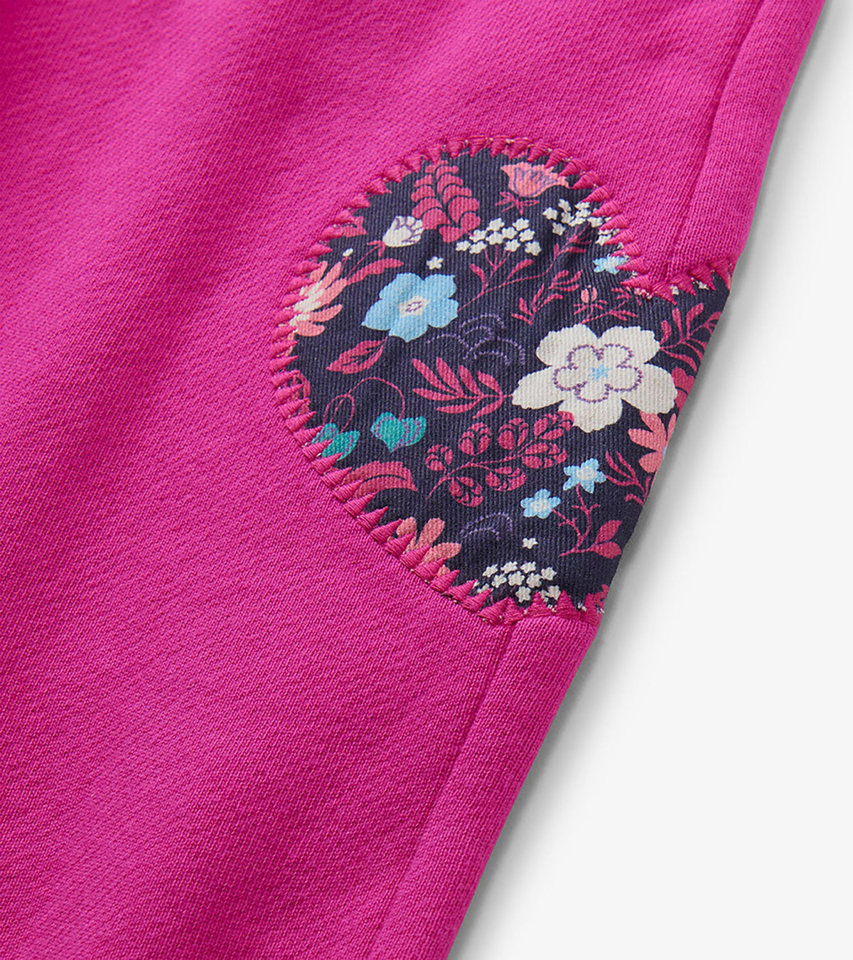 Close-up of the floral heart patch on berry pink wide leg track pants with pink whipstitch edging